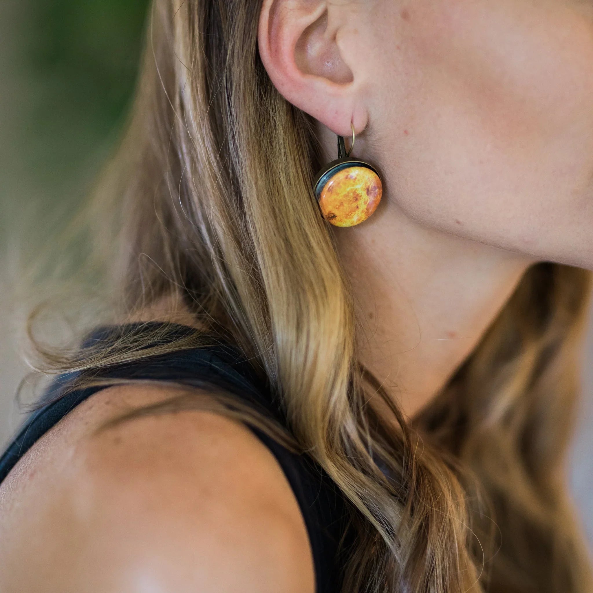 Close-up of woman wearing yellow planet-themed round earrings with gold hooks