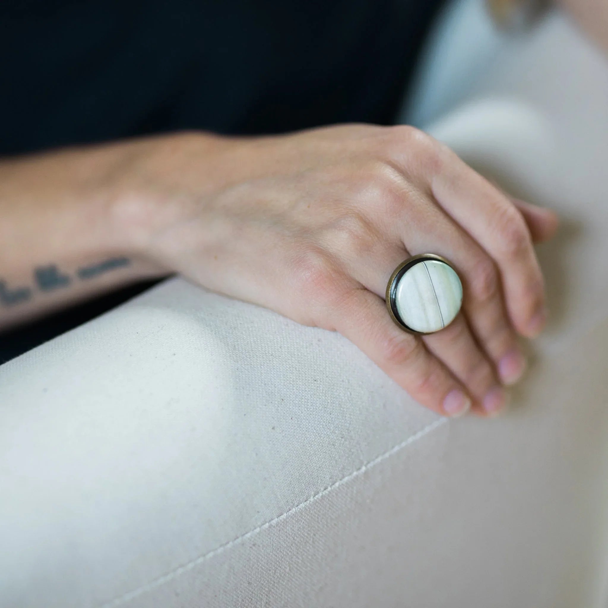 Close-up of a hand wearing a round white stone ring resting on a light fabric surface