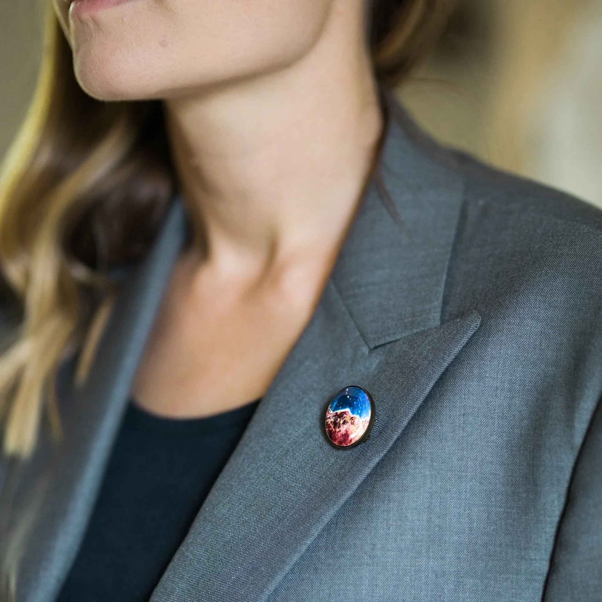 Close-up of woman wearing grey blazer with colorful celestial pin featuring space and stars
