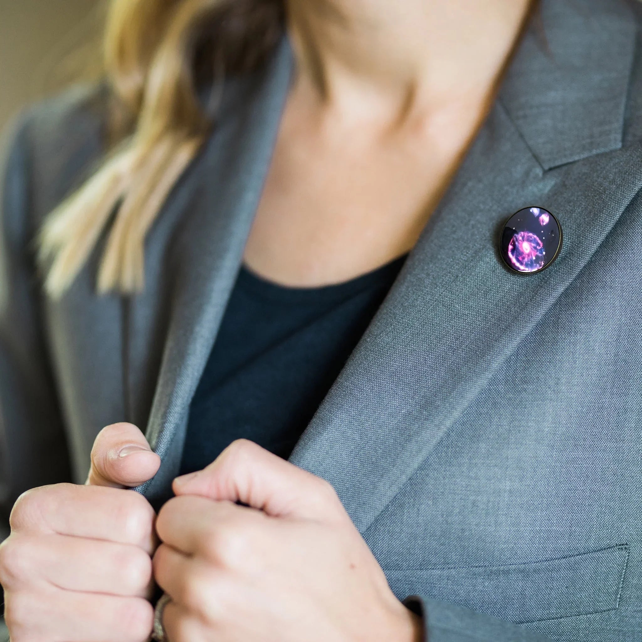 Woman in gray blazer wearing a round cosmic galaxy lapel pin, holding jacket lapels