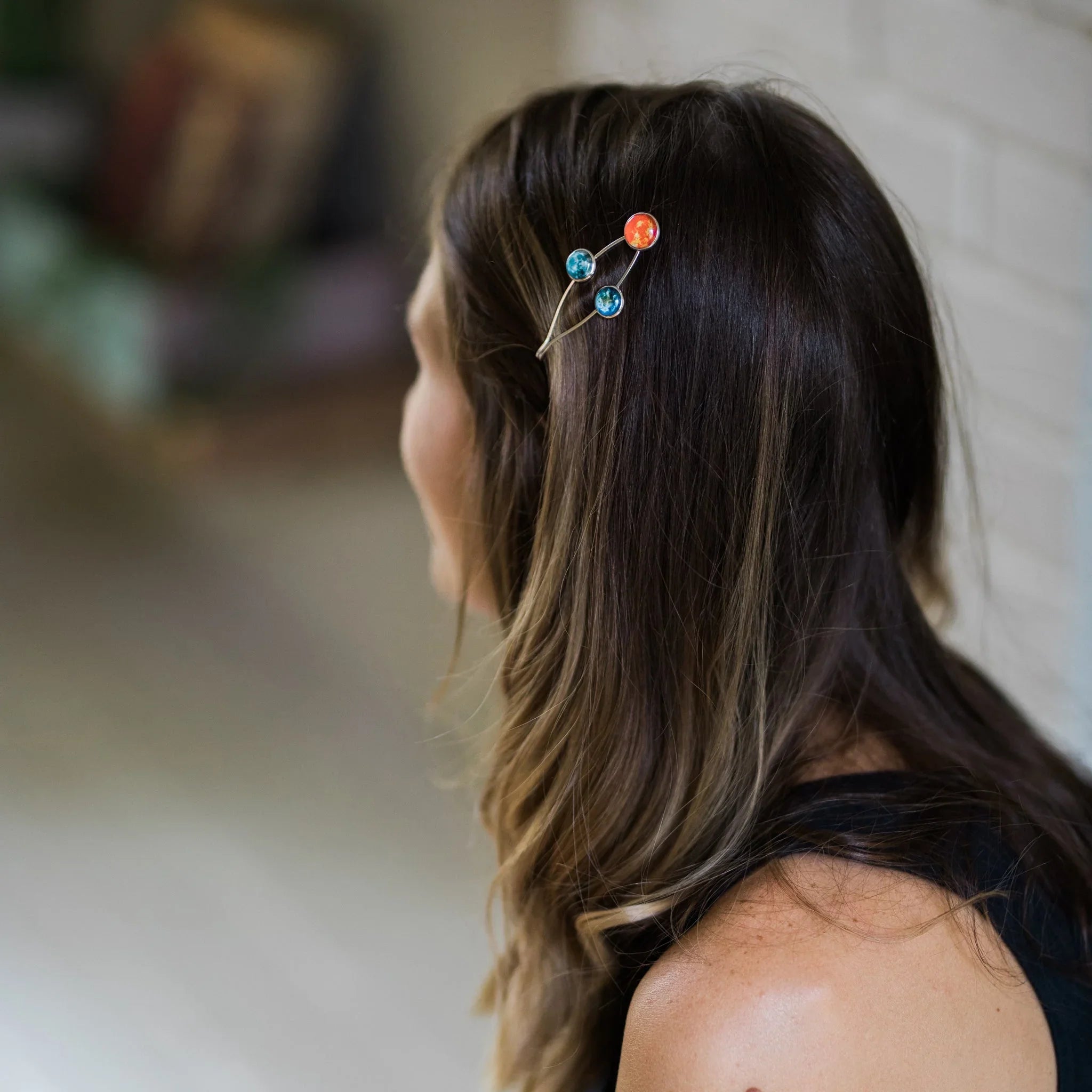Woman with long brown hair wearing a celestial planet-themed hair clip indoors
