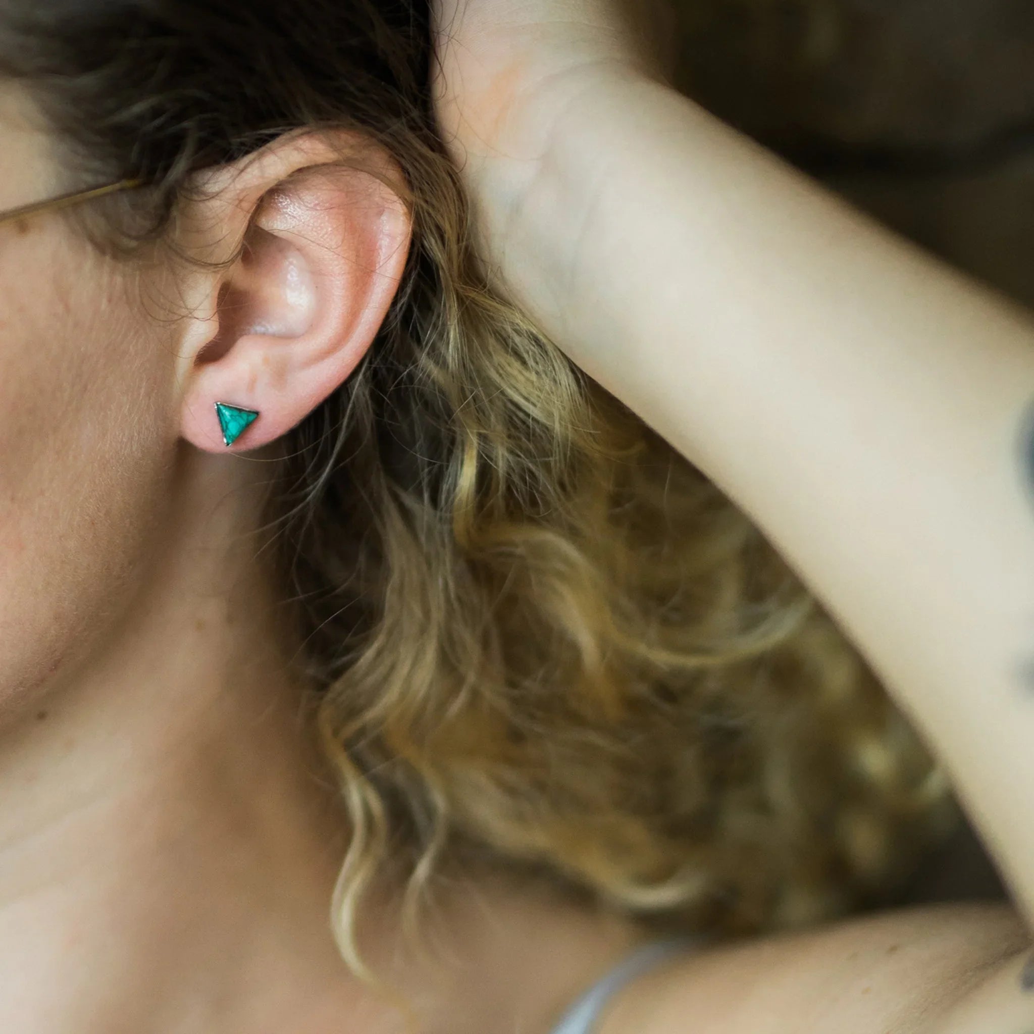Close-up of a woman wearing a green triangle stud earring, curly hair, Qu!rk Boutique