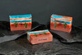 Three artisanal Desert Sunset soaps with layered blue, orange, white colors and cactus design on black stone