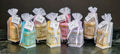 Assorted colorful goat's milk olive oil soaps in white organza gift bags with tags on marble surface