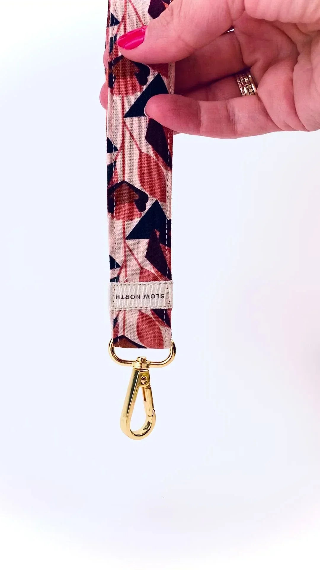 Hand holding pink and brown patterned fabric keychain with gold metal clasp and Slow North label