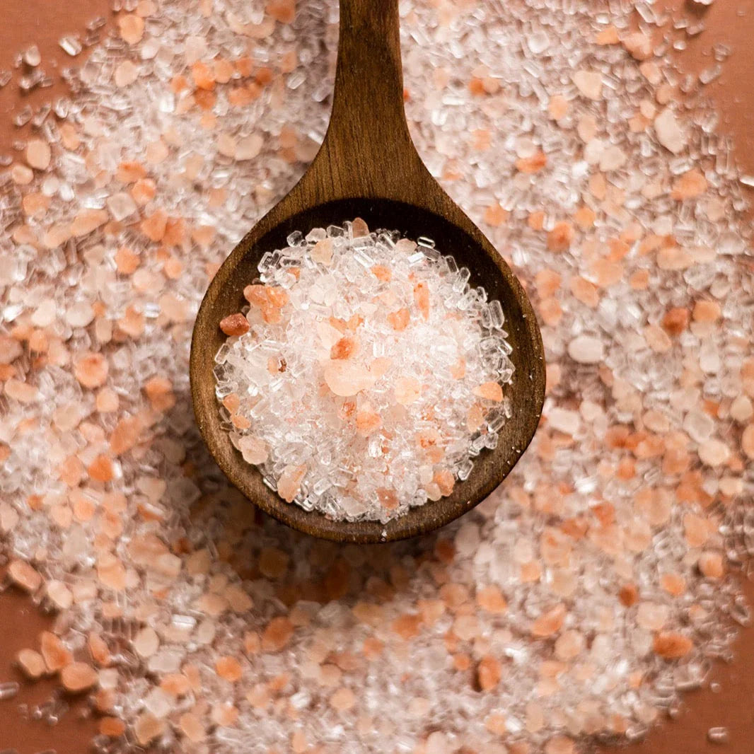 Close-up of pink Himalayan bath salt crystals in a wooden spoon on a bed of salts