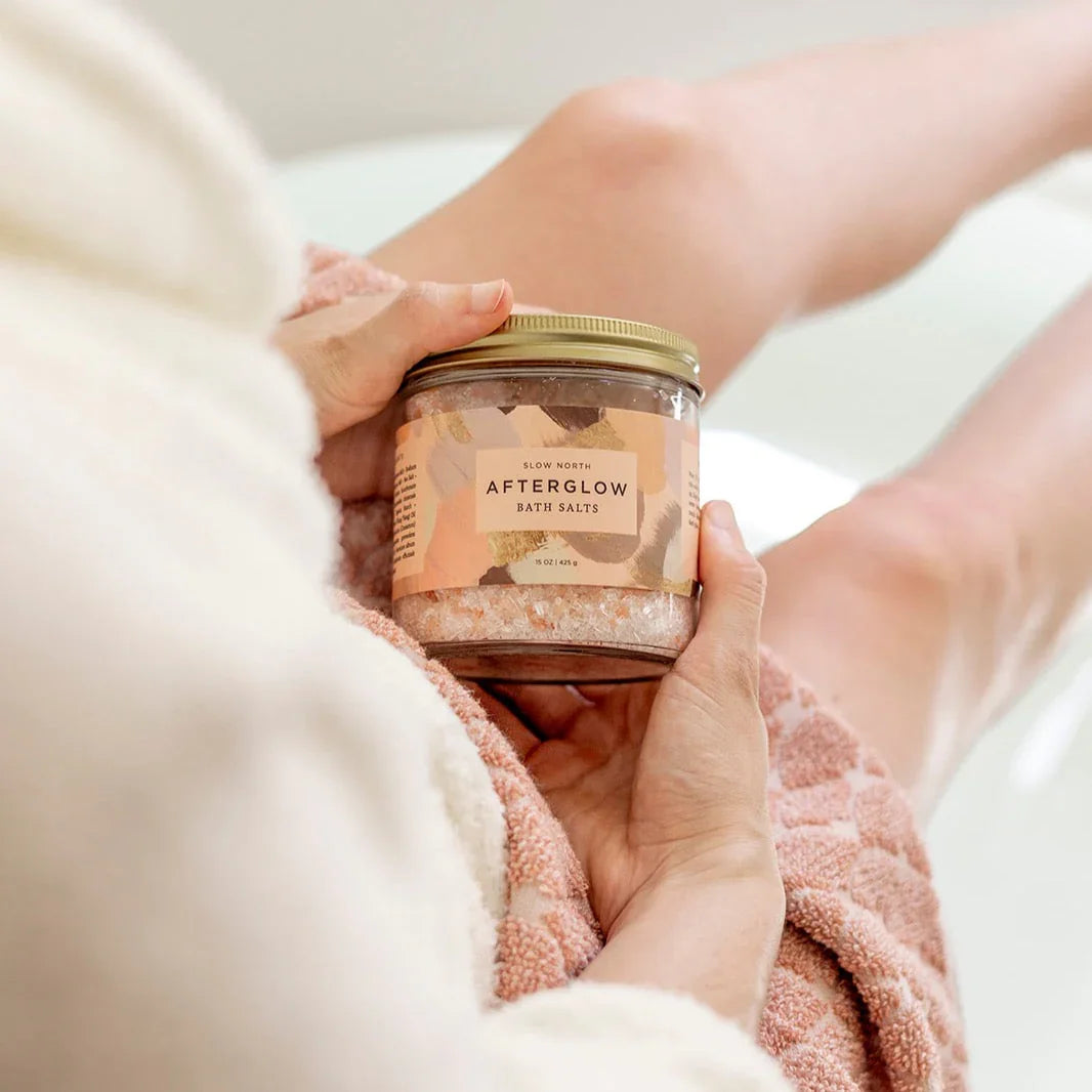 Person holding Slow North Afterglow bath salts jar while sitting with legs stretched out