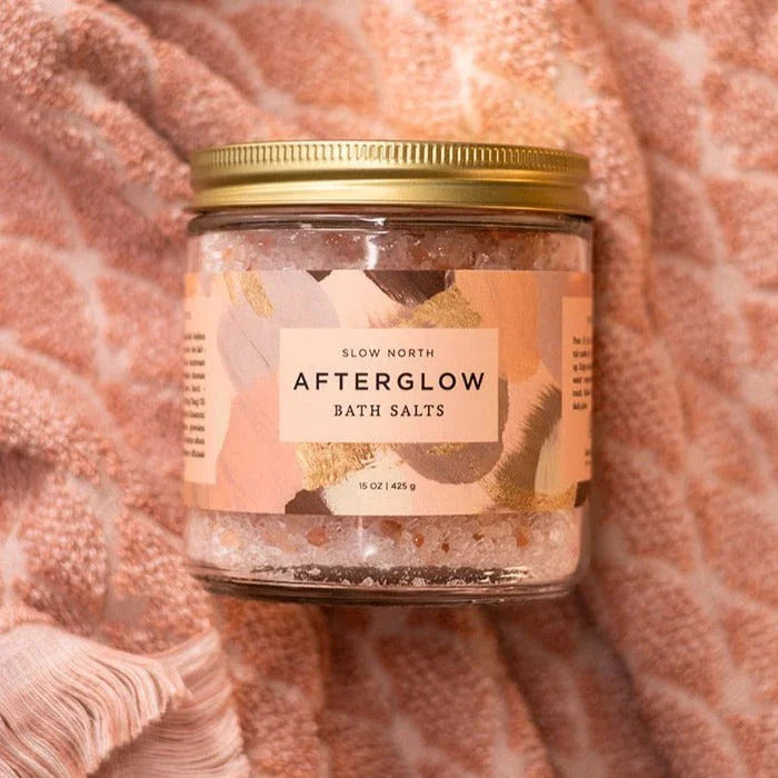 Jar of Slow North Afterglow bath salts with gold lid on textured pink fabric