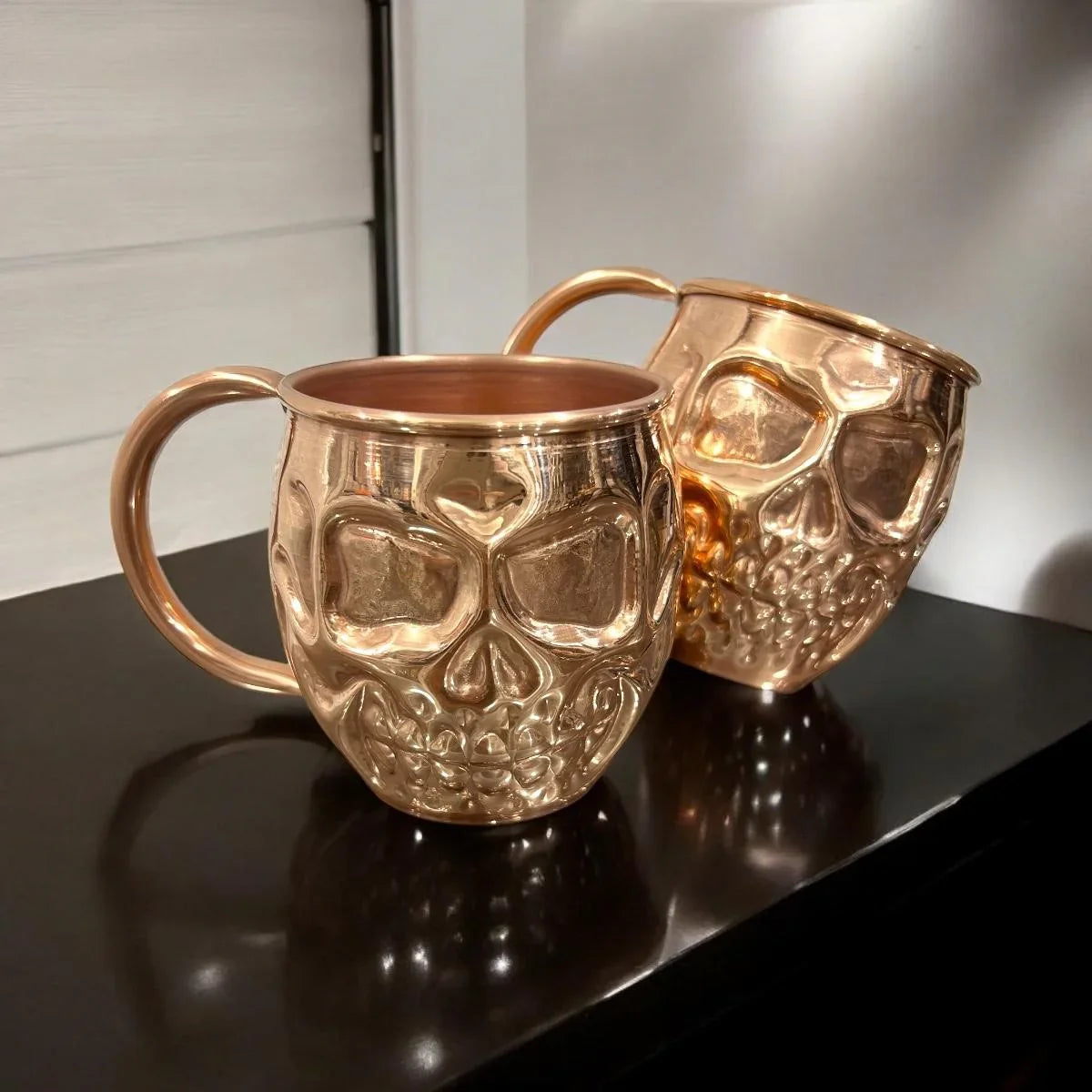 Two metallic skull-shaped mugs on a dark counter at Qu!rk Boutique gift shop