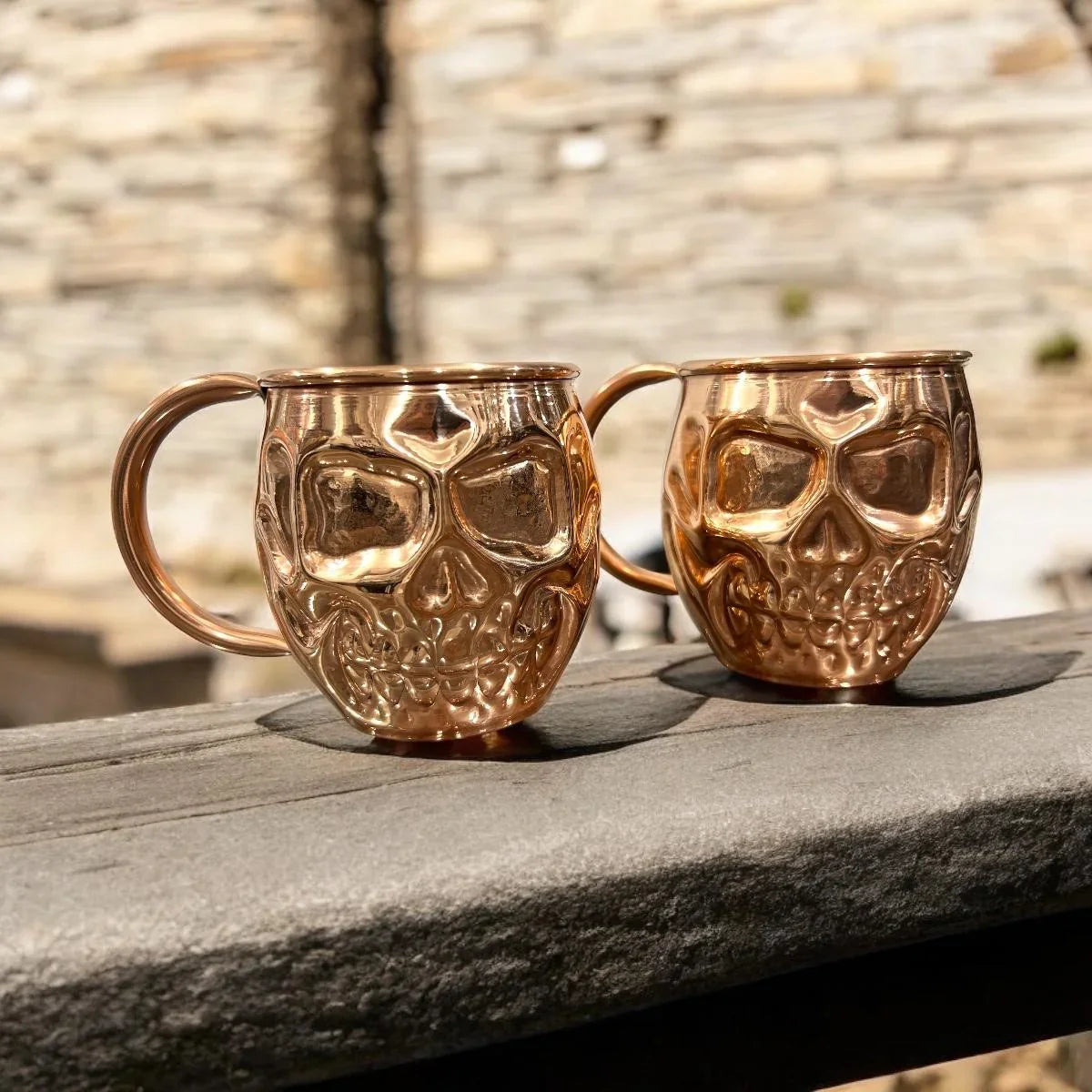 Two metallic skull mugs on a rustic wooden surface, artisan giftware from Qu!rk Boutique