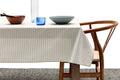 Minimalist dining setup with striped tablecloth, wooden bowl, blue glass, gray bowl, and modern wood chair