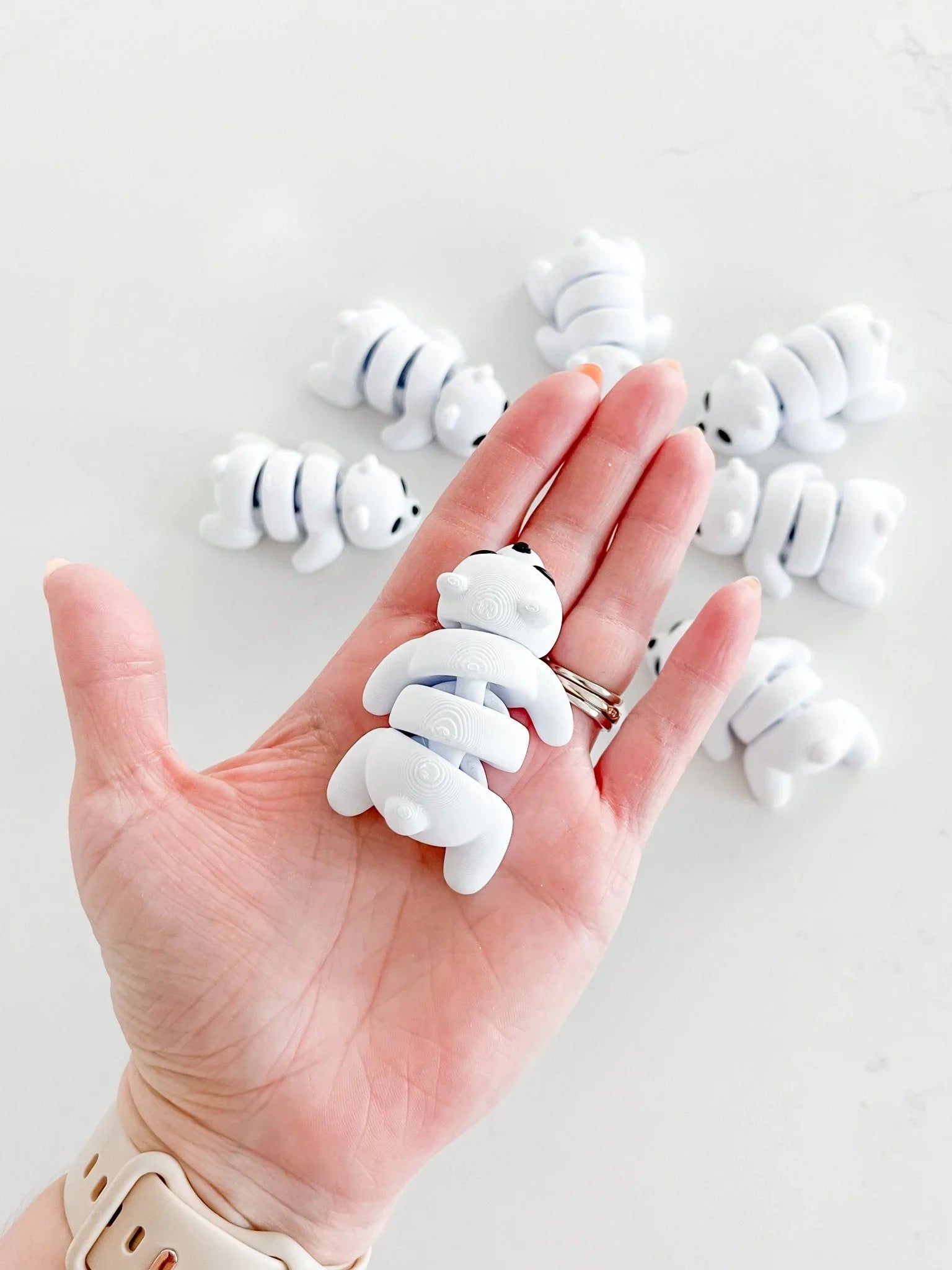 Hand holding a white bear-shaped fidget toy with more bear fidgets on a white surface