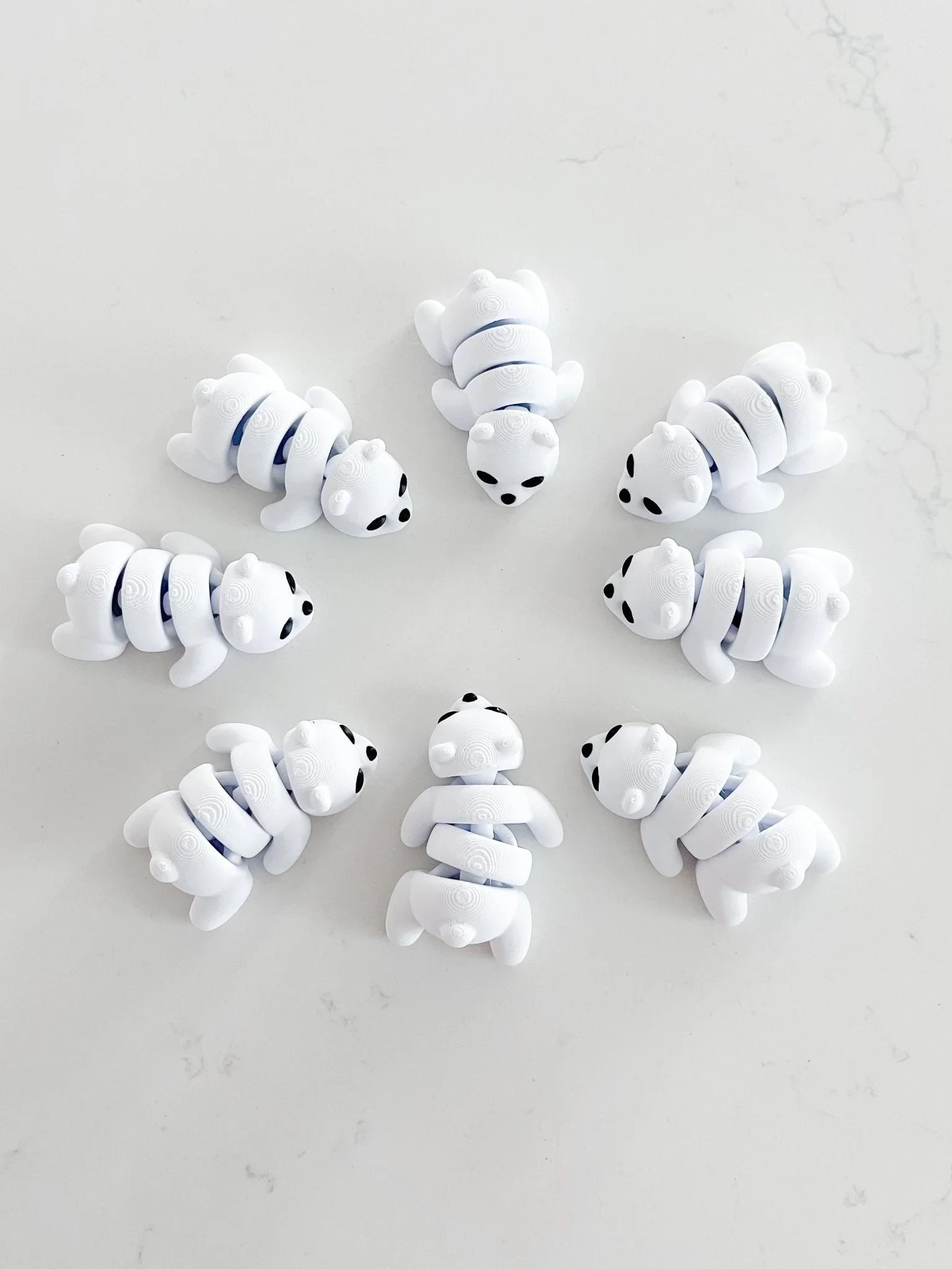 Eight white baby bear fidget toys arranged in a circle on a marble surface at Qu!rk Boutique