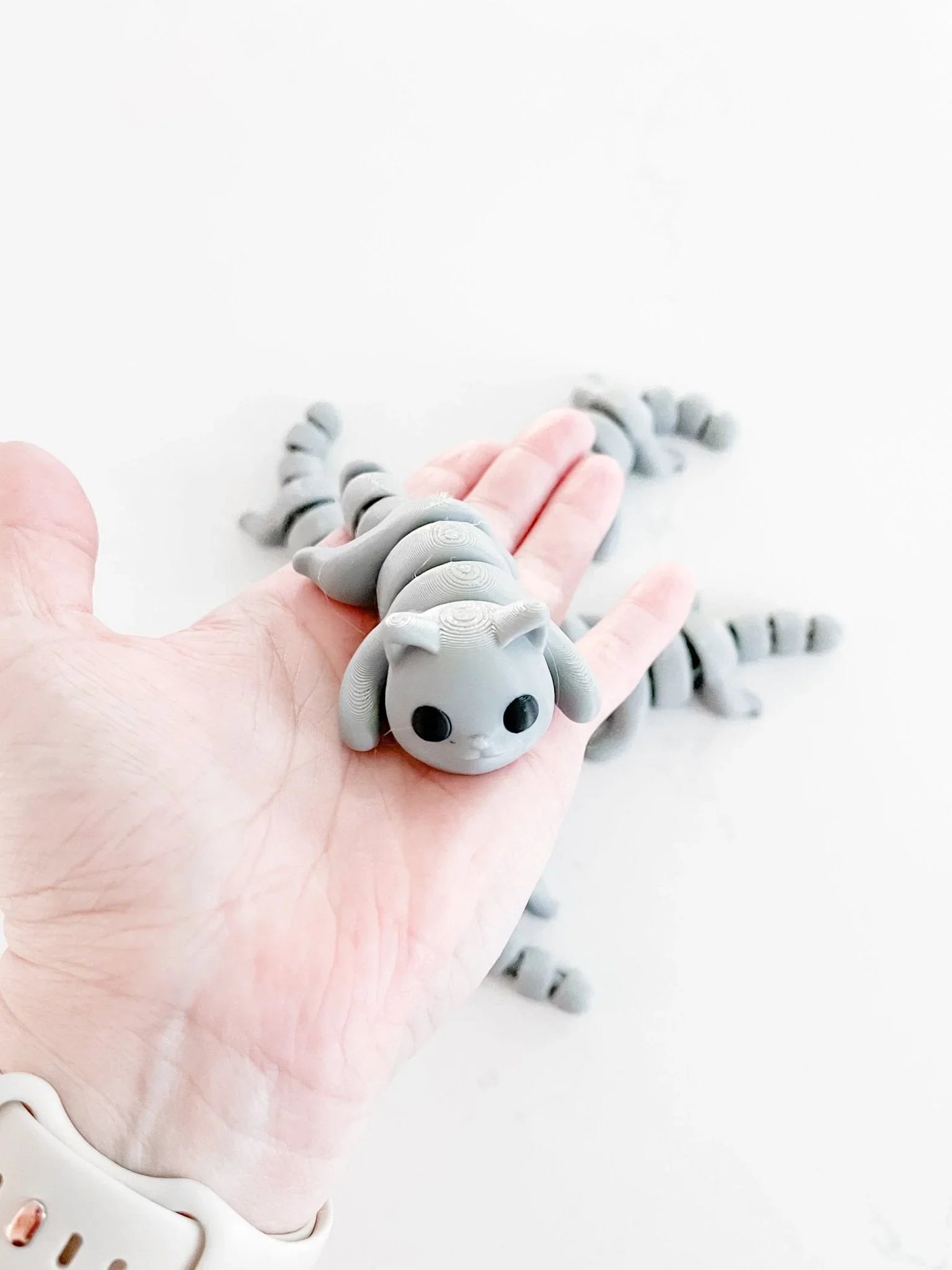Gray articulated cat fidget toy in a hand, playful boutique gift, minimalist white background