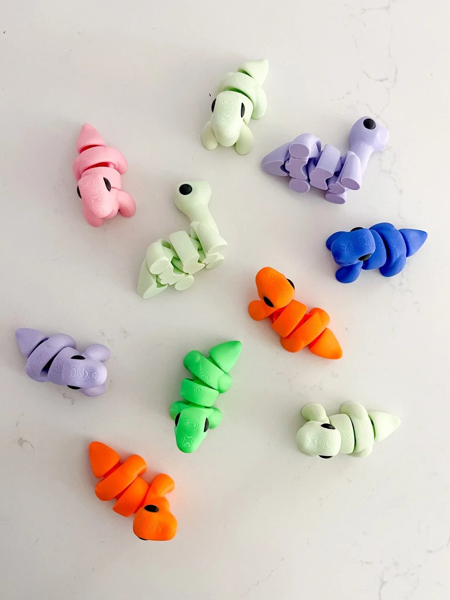 Colorful baby dinosaur fidget toys on white background at Qu!rk Boutique, artist-designed gifts
