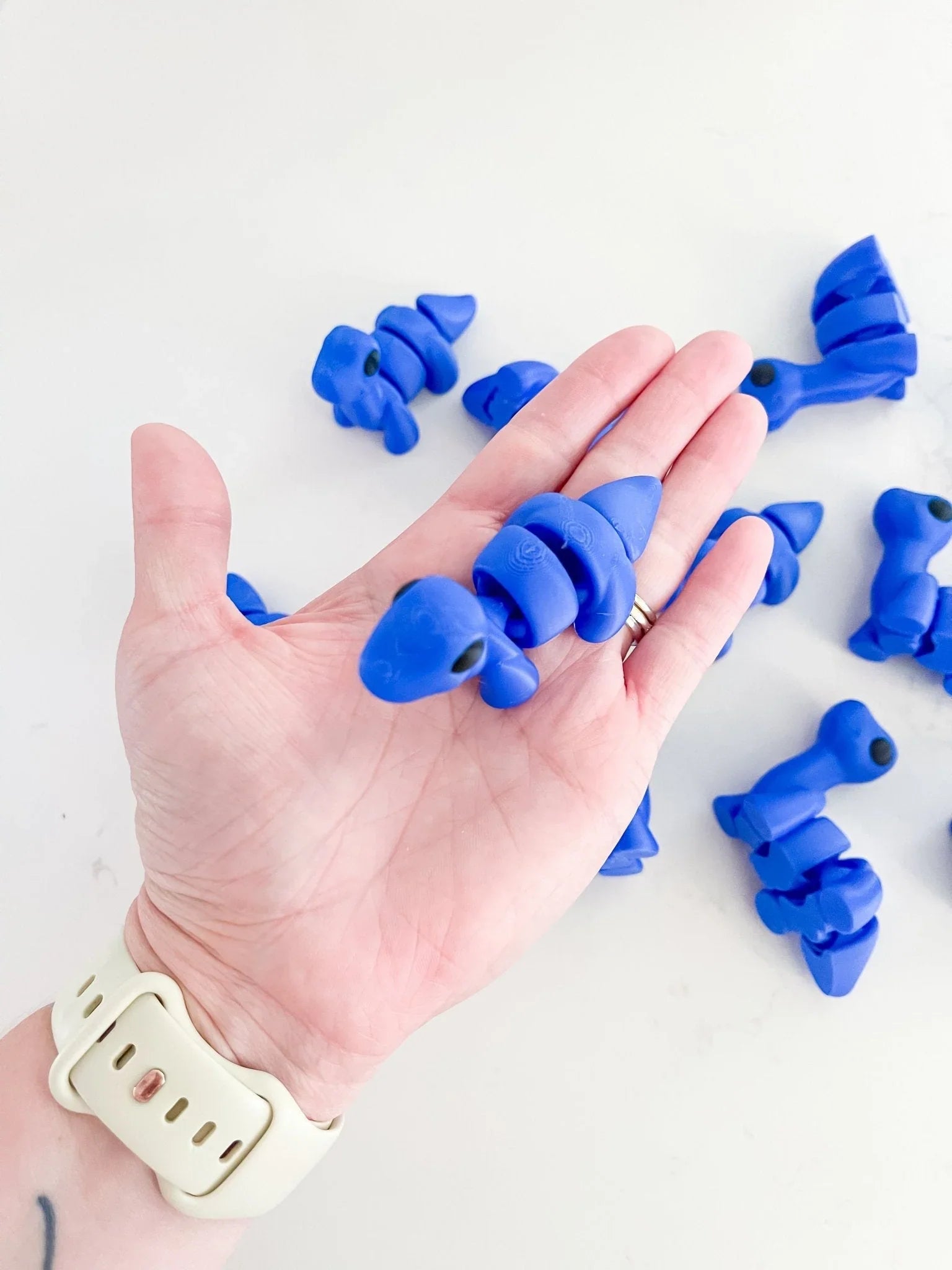 Hand holding a royal blue baby dinosaur fidget toy, quirky artist-designed gift from Qu!rk Boutique