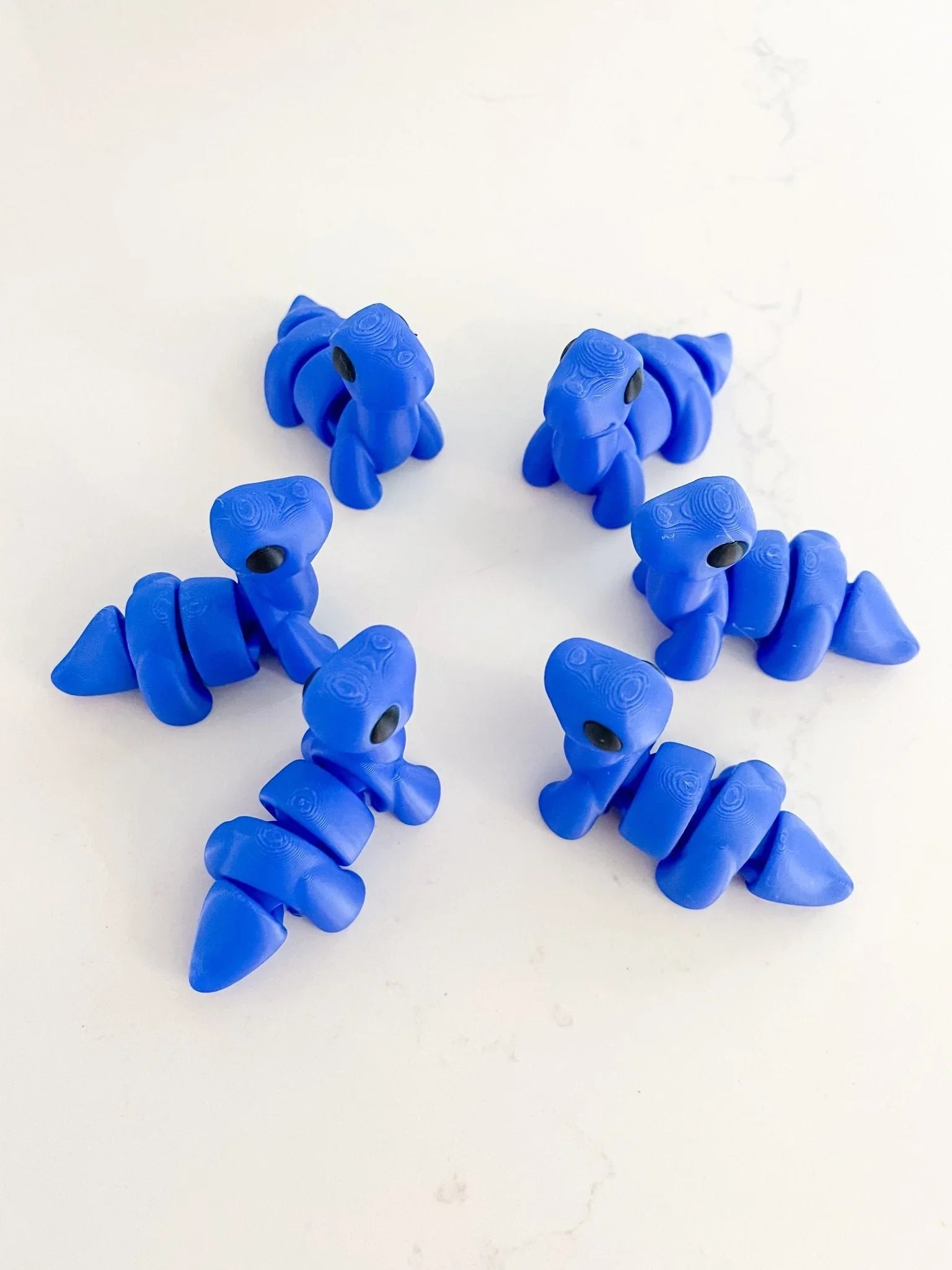 Six royal blue baby dinosaur fidget toys on a white background at Qu!rk Boutique & Gift Shop