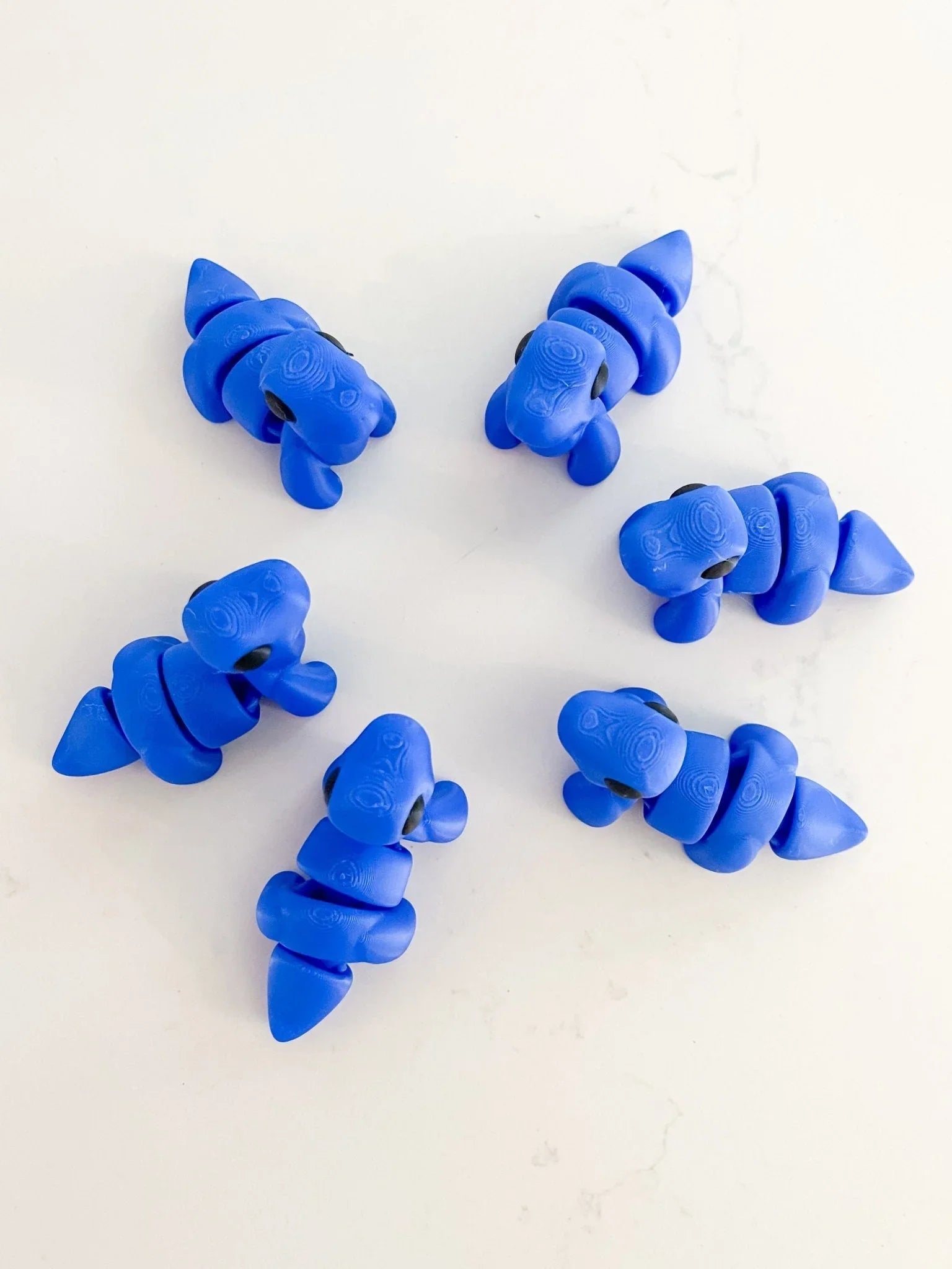 Six royal blue baby dinosaur fidget toys on a white background, quirky boutique gift idea