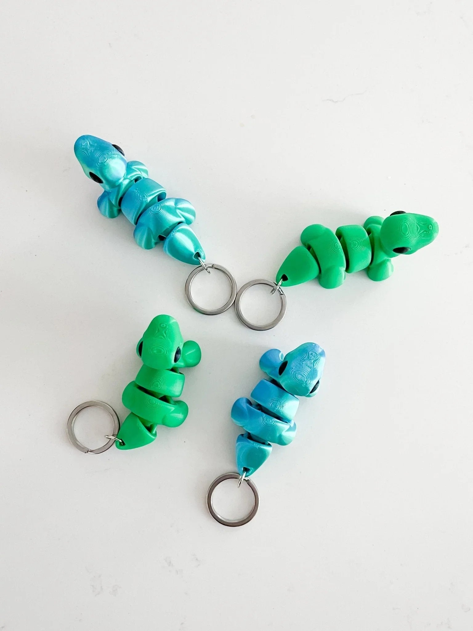 Colorful baby dinosaur keychains in green and blue on a white background from Qu!rk Boutique