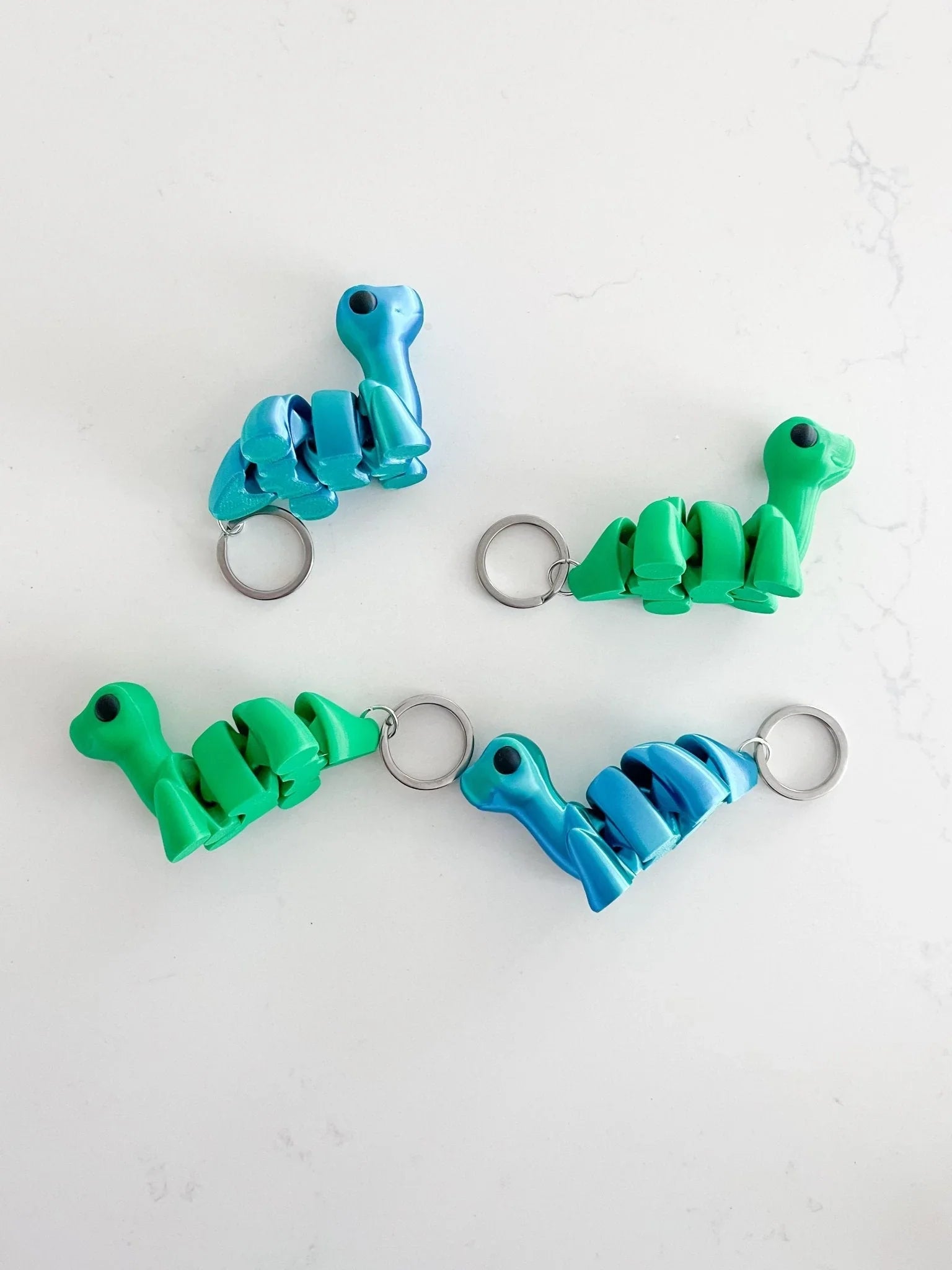 Assorted green and blue baby dinosaur keychains on a white background at Qu!rk Boutique.