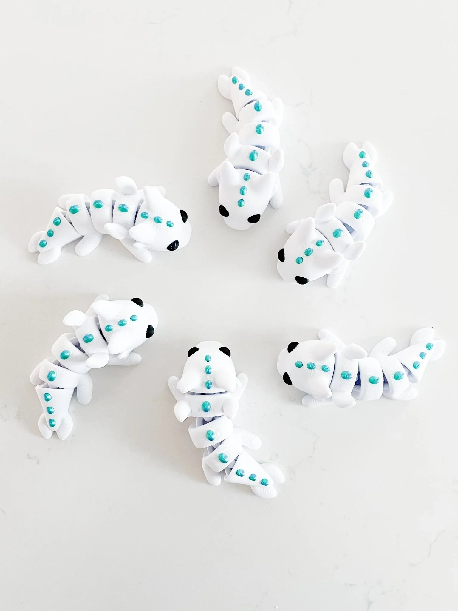White baby dragon fidget toys with teal accents on a white background at Qu!rk Boutique