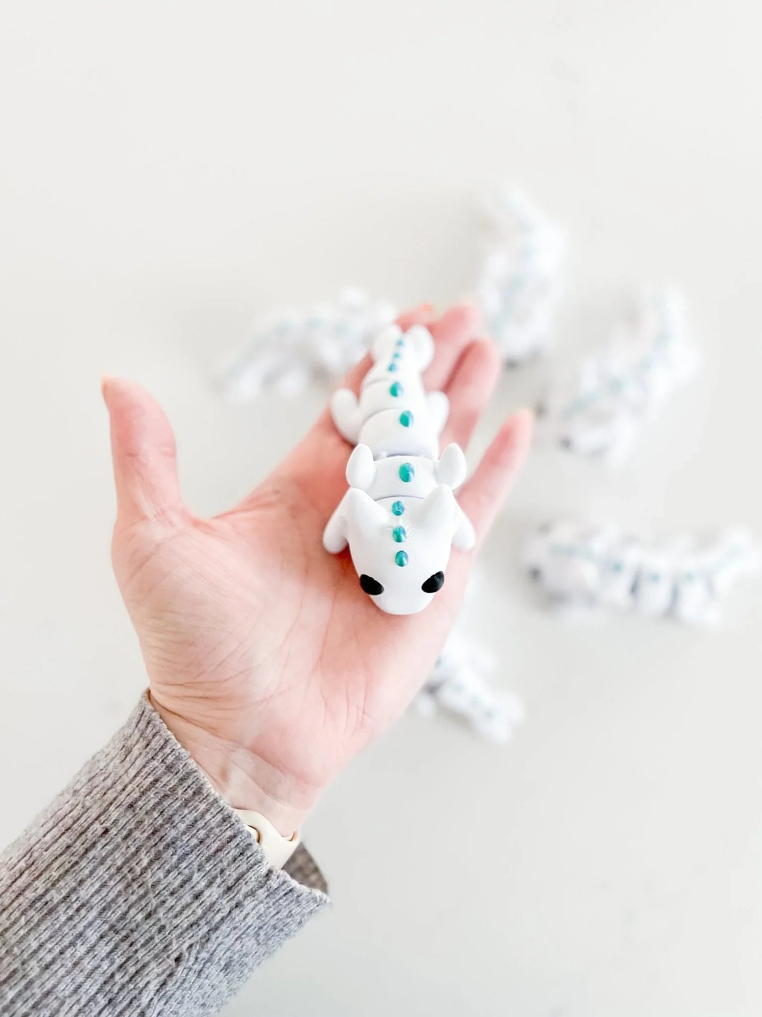 Hand holding a white baby dragon fidget toy with teal spots, whimsical gift at Qu!rk Boutique