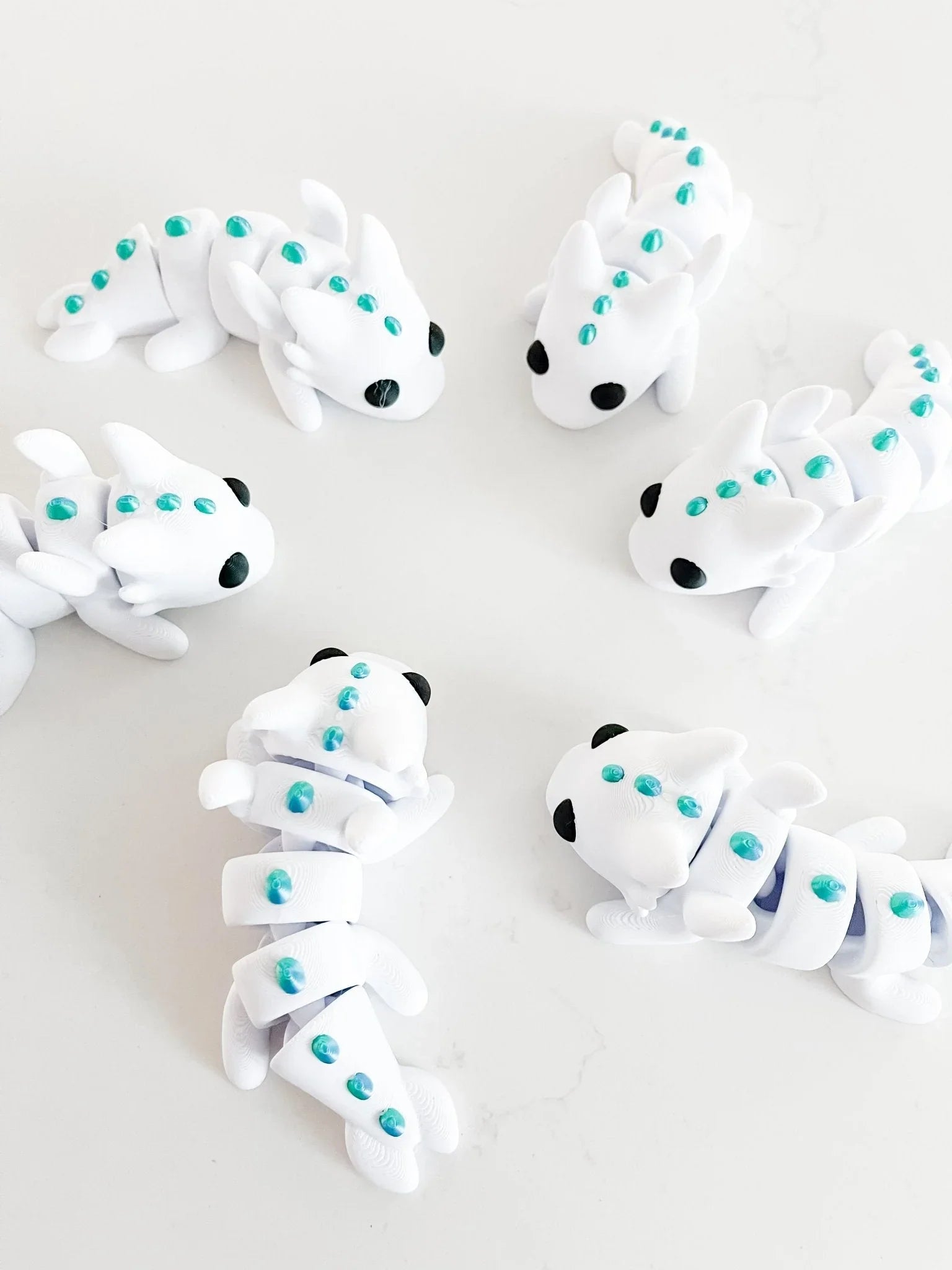 White baby dragon fidget toys with teal spots arranged on a white surface at Qu!rk Boutique
