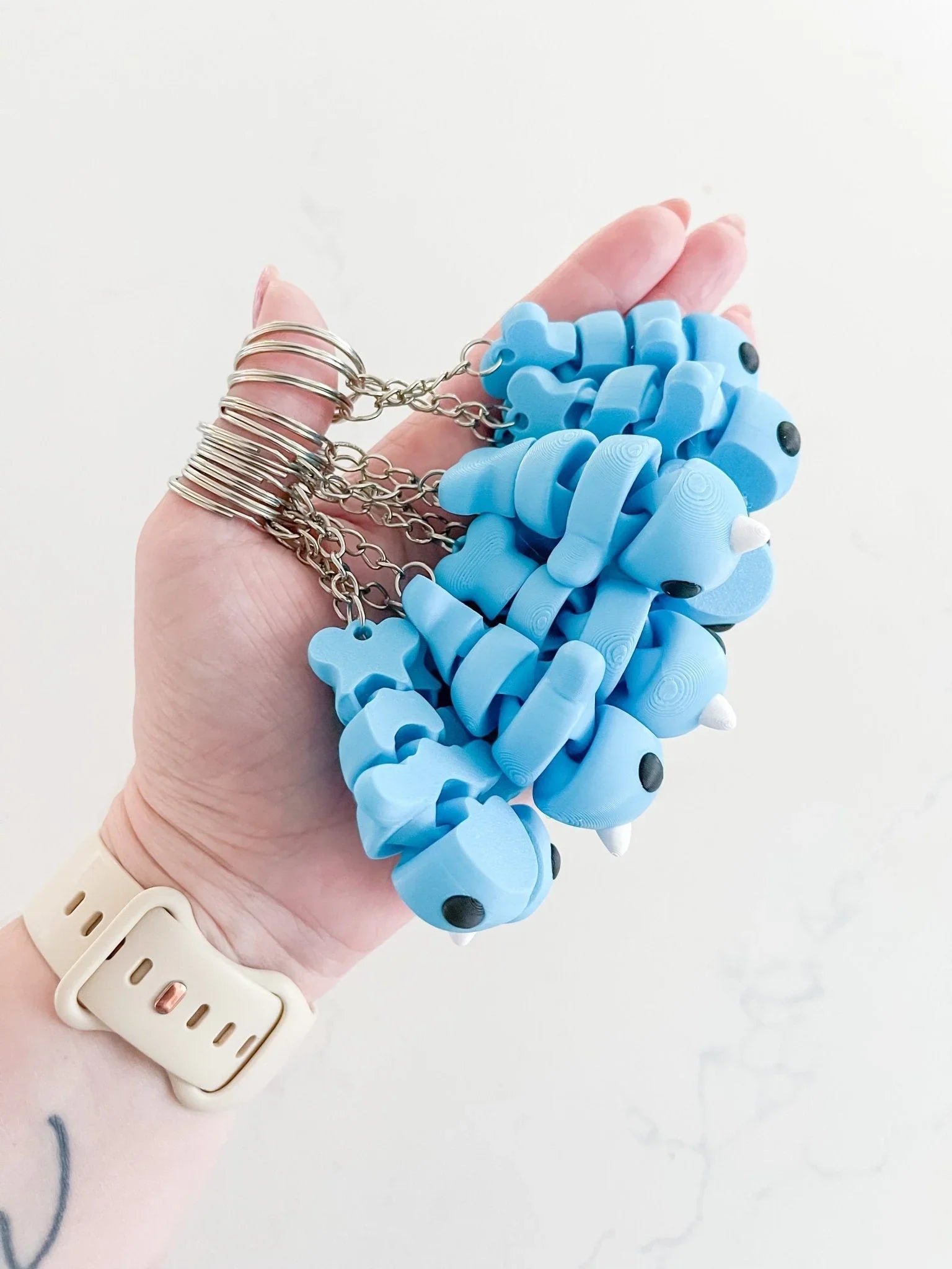 Hand holding several blue baby narwhal keychains with silver chains, Qu!rk Boutique gift idea