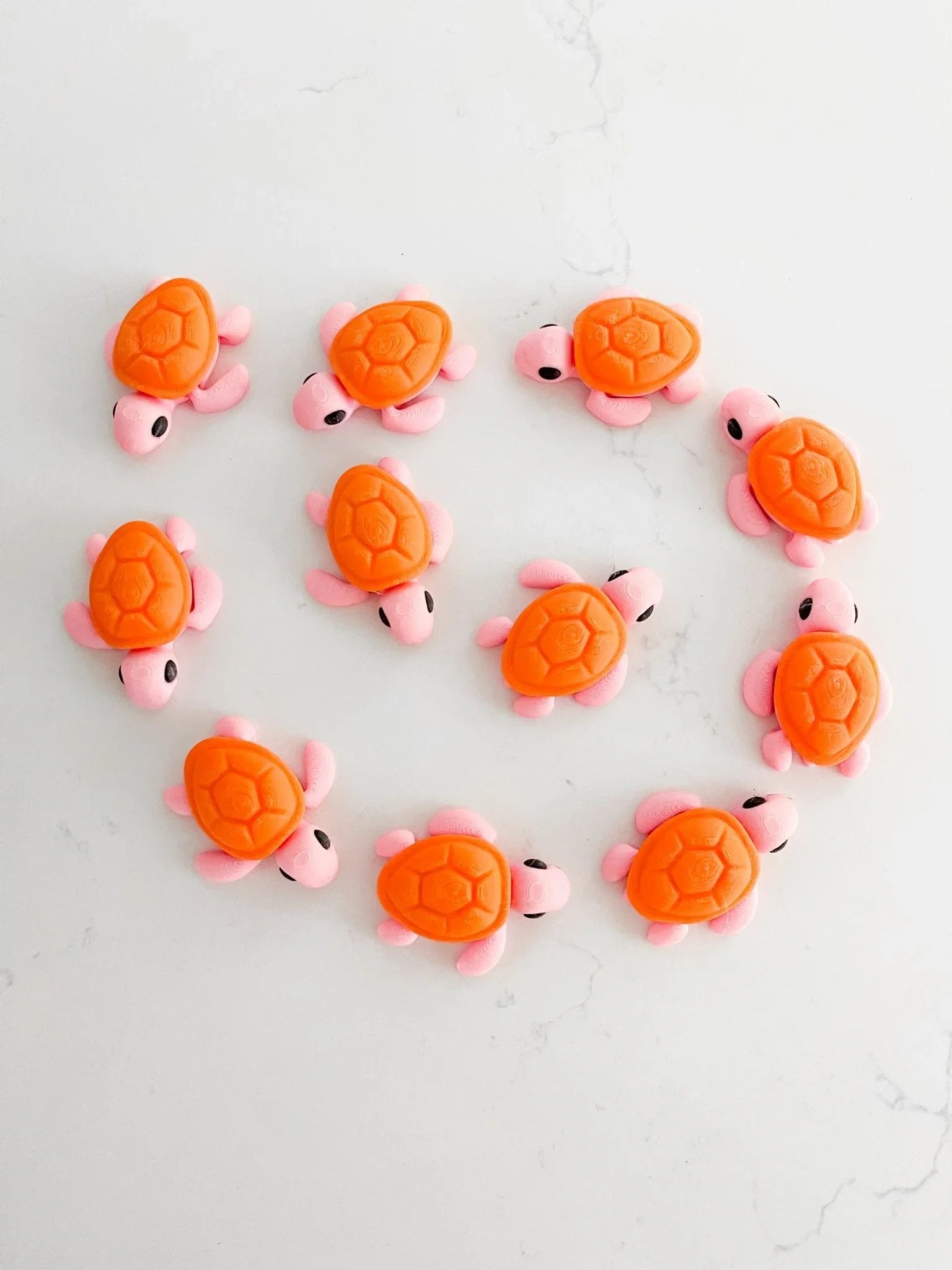 Cute orange and pink baby turtle figurines in a circle on a white marble surface, Qu!rk Boutique gift