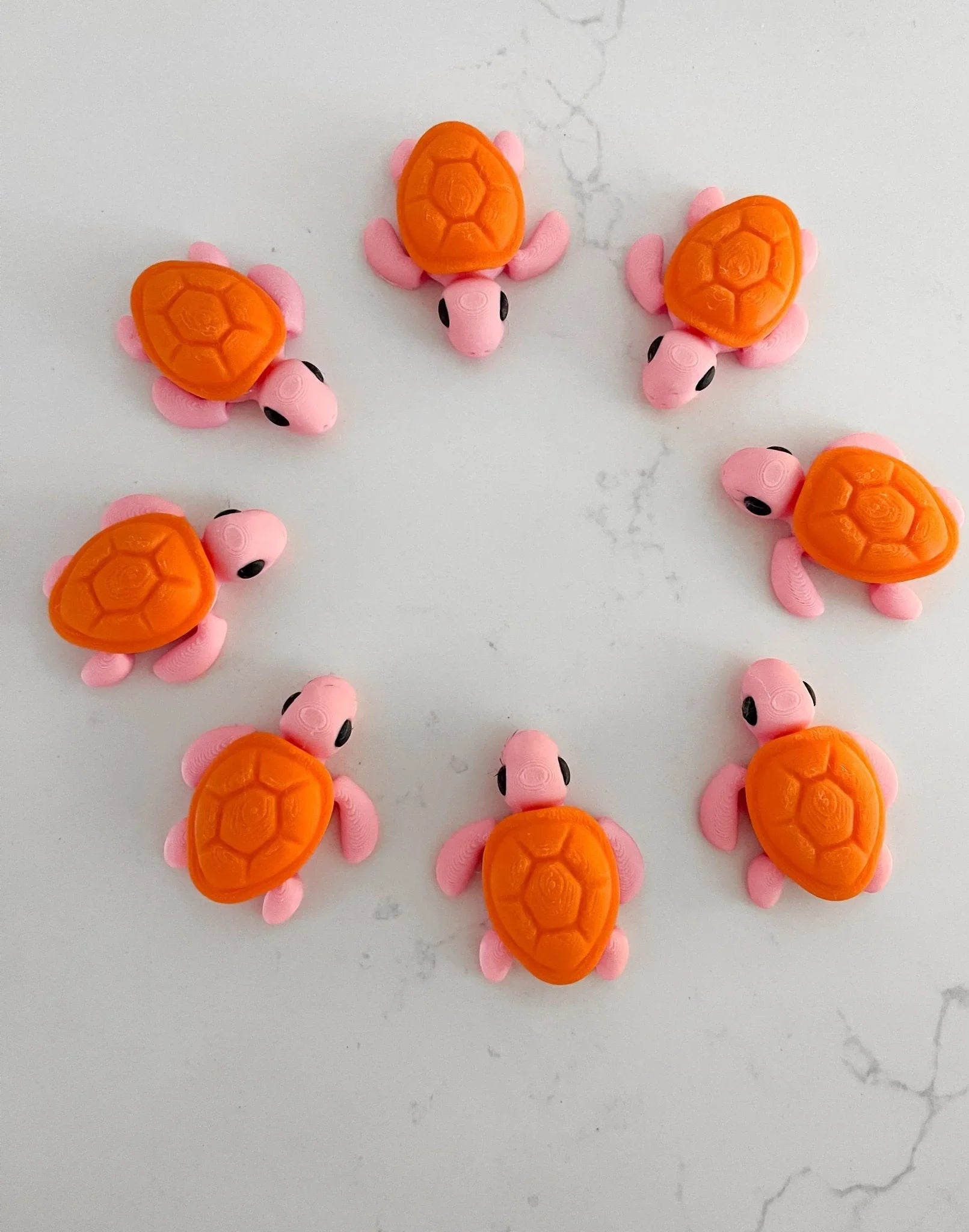 Cute pink and orange baby turtle figurines in a circle on white marble, Qu!rk Boutique gift