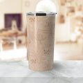 Beige insulated travel tumbler with floral leaf pattern on marble countertop in cozy room
