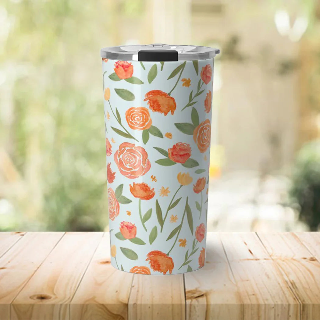 Floral-patterned stainless steel tumbler with lid on wooden table in bright indoor setting