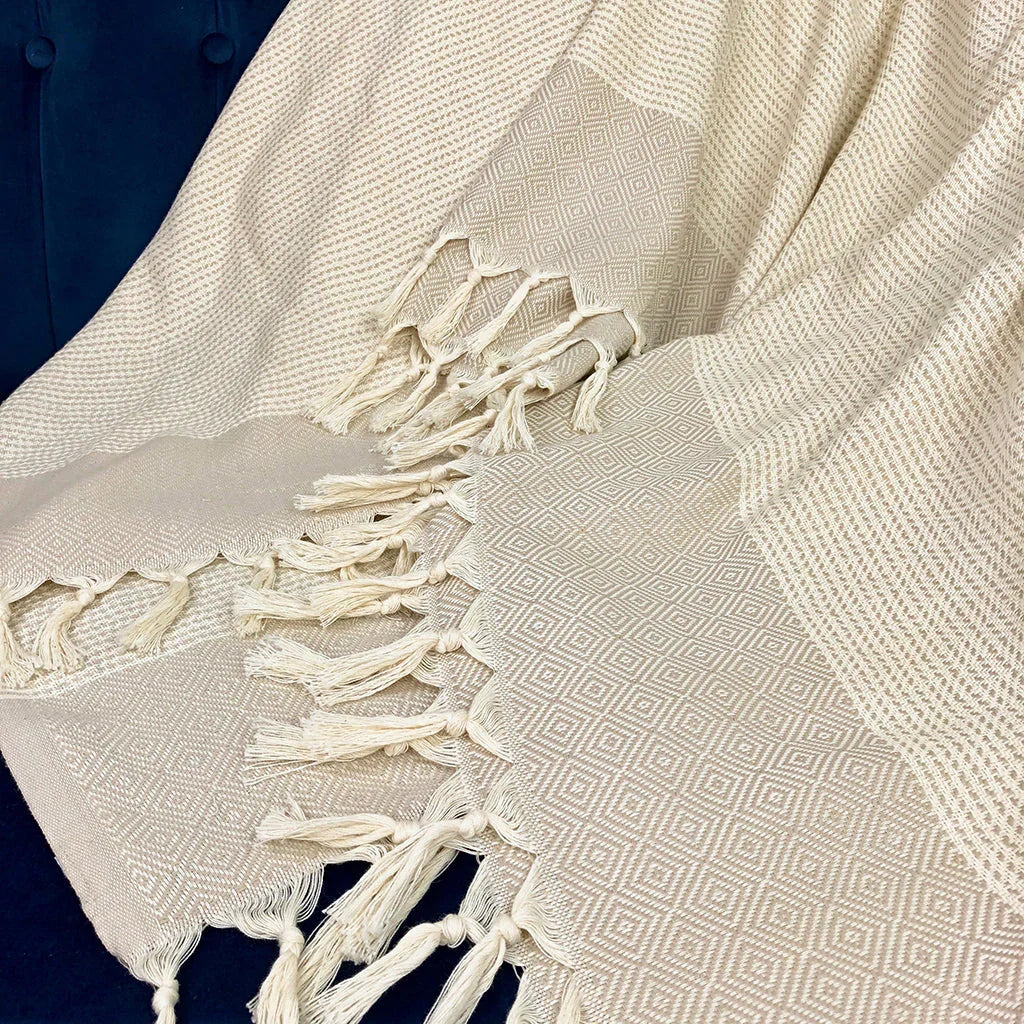 Beige diamond-pattern throw blanket with fringed edges, draped on a dark surface.