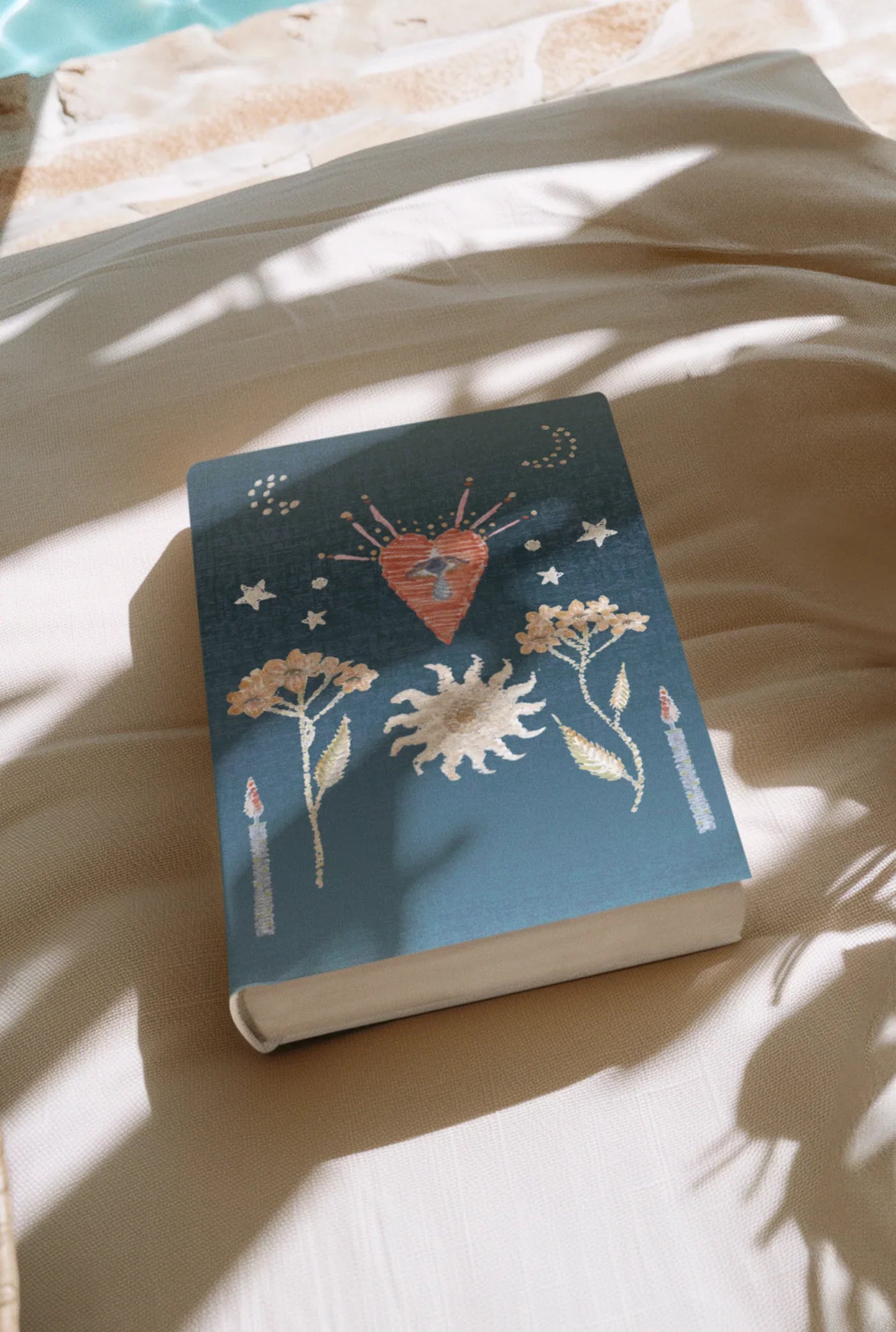 Blue book with mystical heart, sun, flowers, stars, and candle illustrations on white fabric