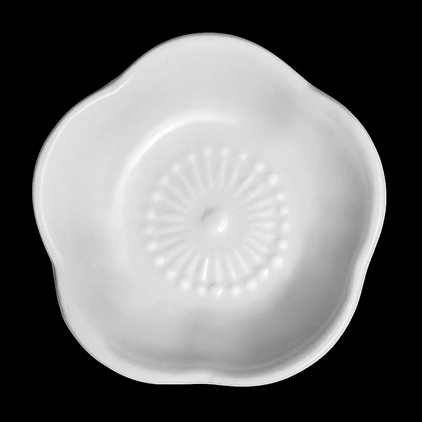 White ceramic flower-shaped dish with textured center on black background