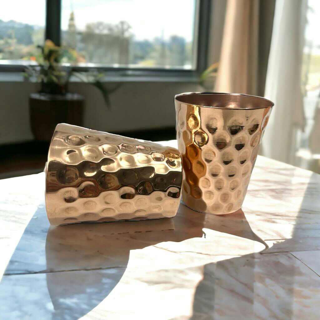 Two hammered copper cups on a marble table, sunlight shining, modern boutique decor