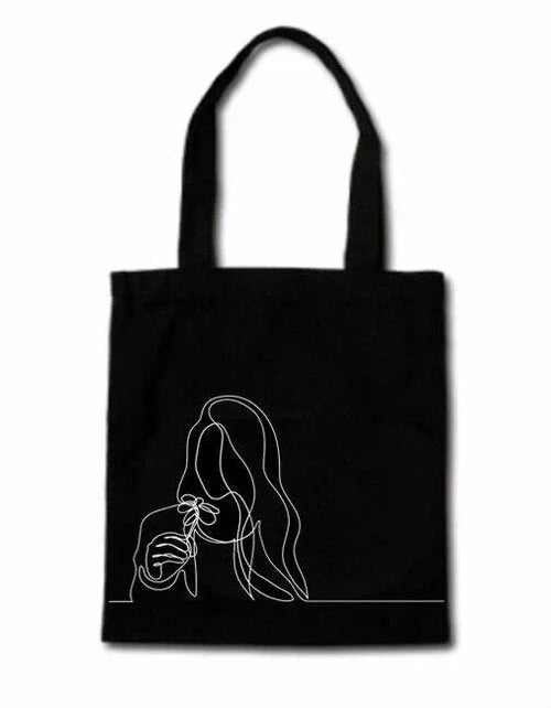Black tote bag with white continuous line art of a woman holding a flower