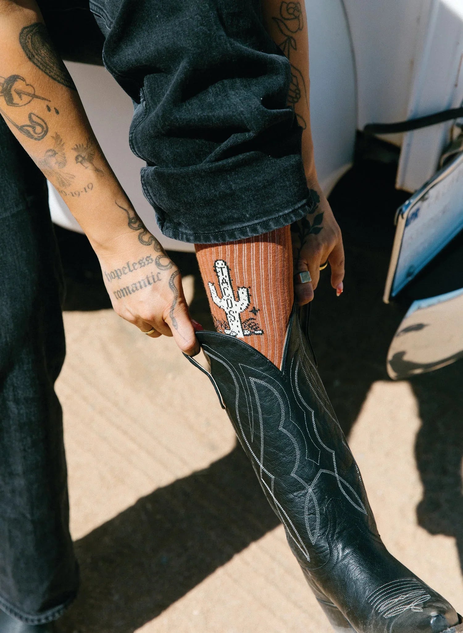 Person wearing rust-colored cactus-themed socks with black cowboy boots outdoors
