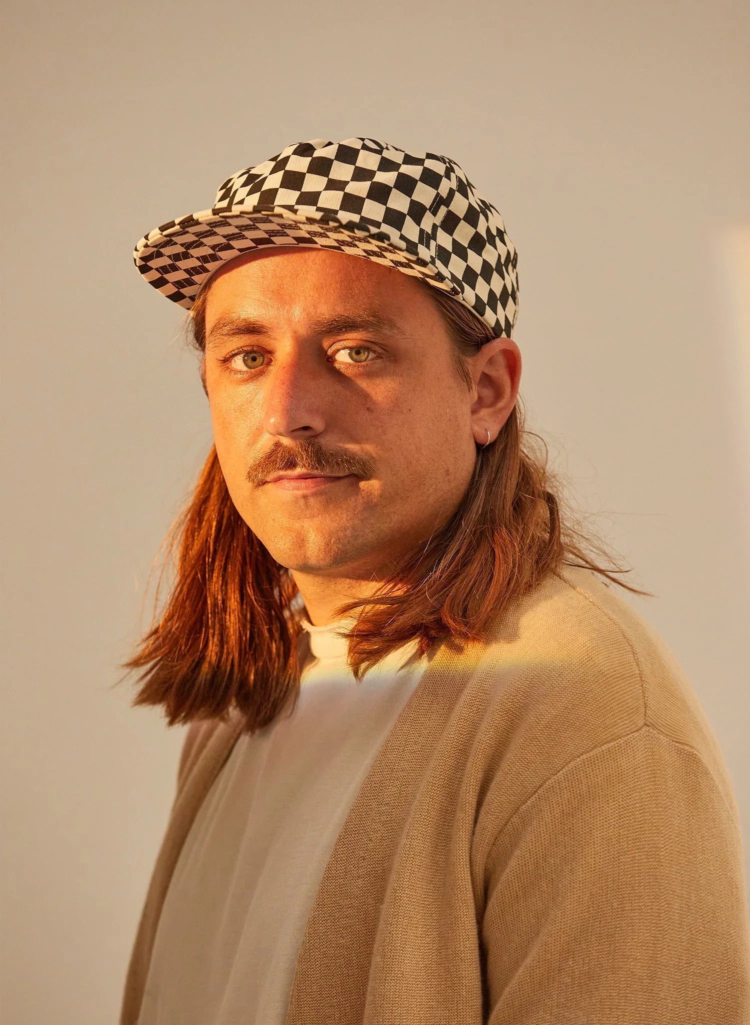 Person in checkerboard black and white hat and beige cardigan, soft golden light, Qu!rk Boutique style