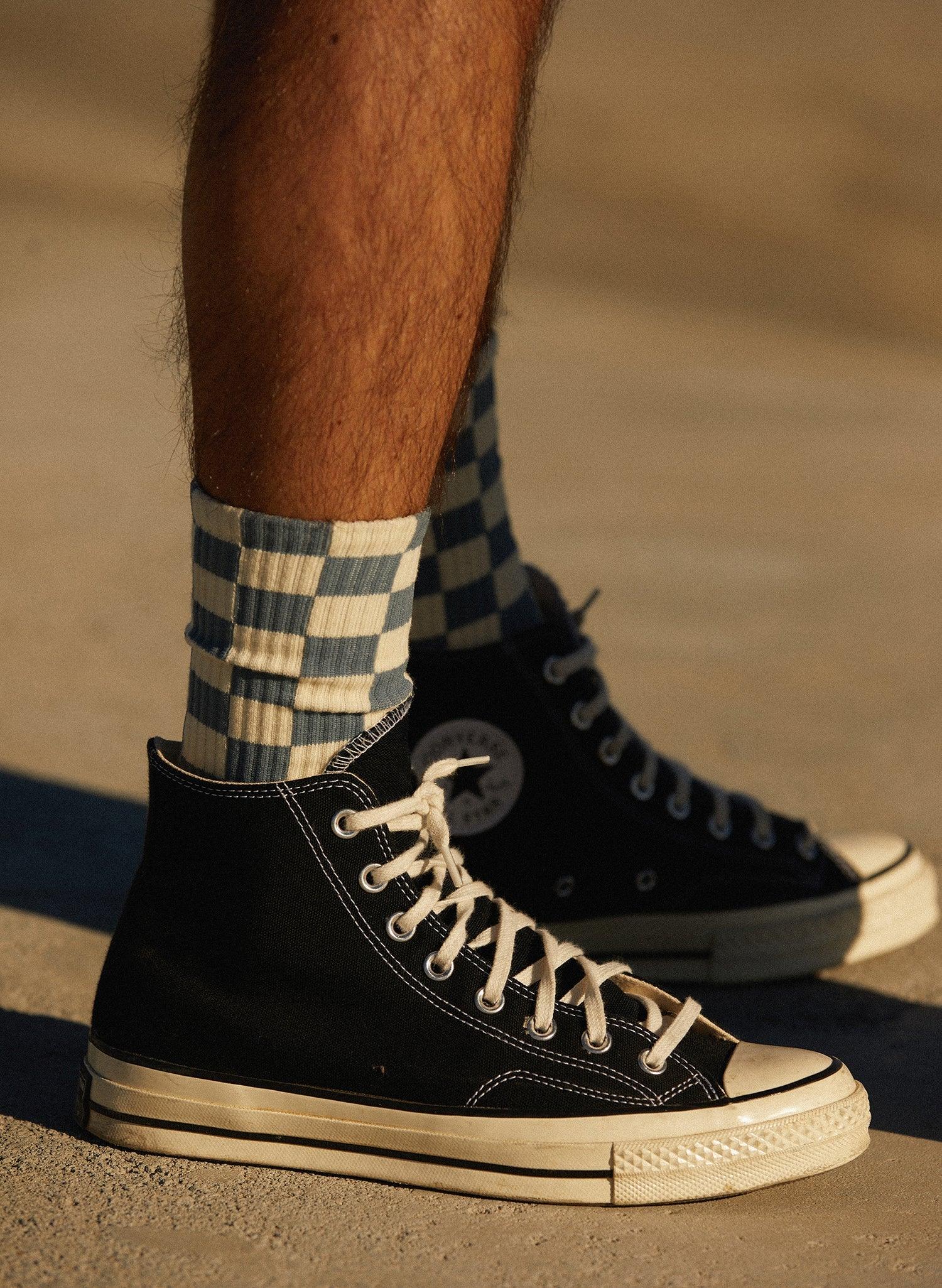 Blue and white checkerboard socks styled with black high-top sneakers on outdoor pavement