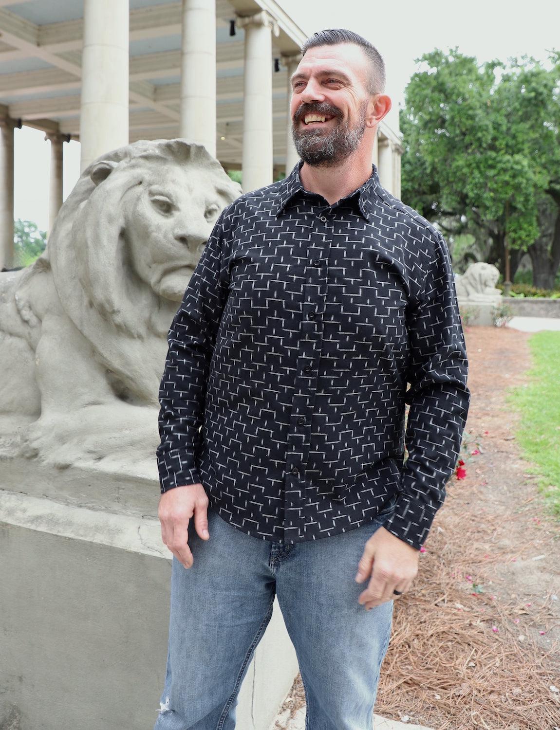 Man wearing a black patterned button-down shirt and jeans near a stone lion statue outdoors