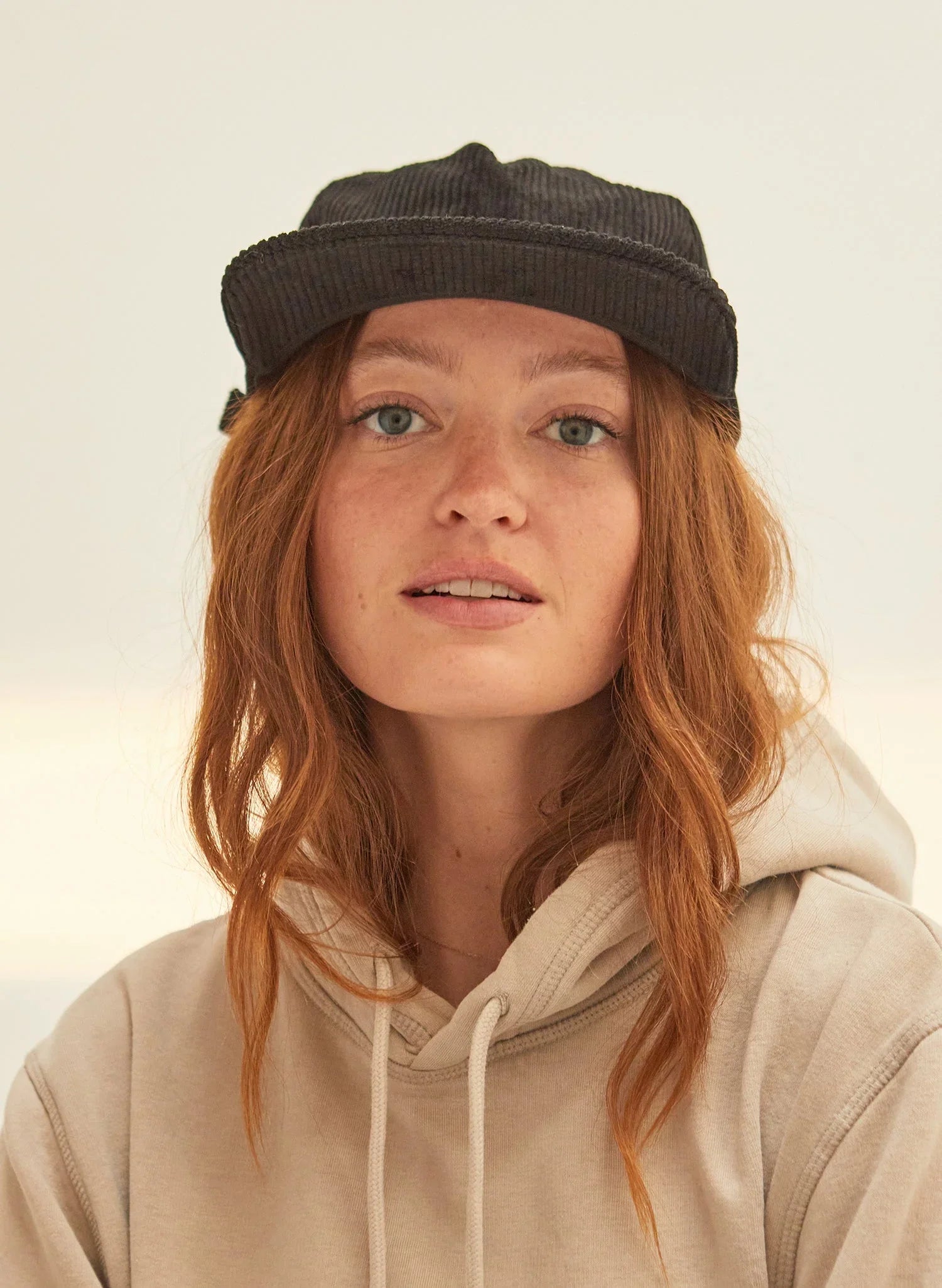 Woman wearing black corduroy cap and beige hoodie, Qu!rk Boutique sustainable fashion