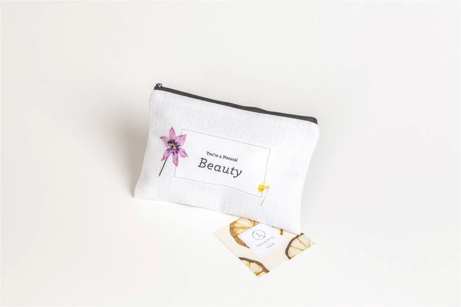 White cosmetic bag with zipper and floral design, text 'You're a Natural Beauty', on white background