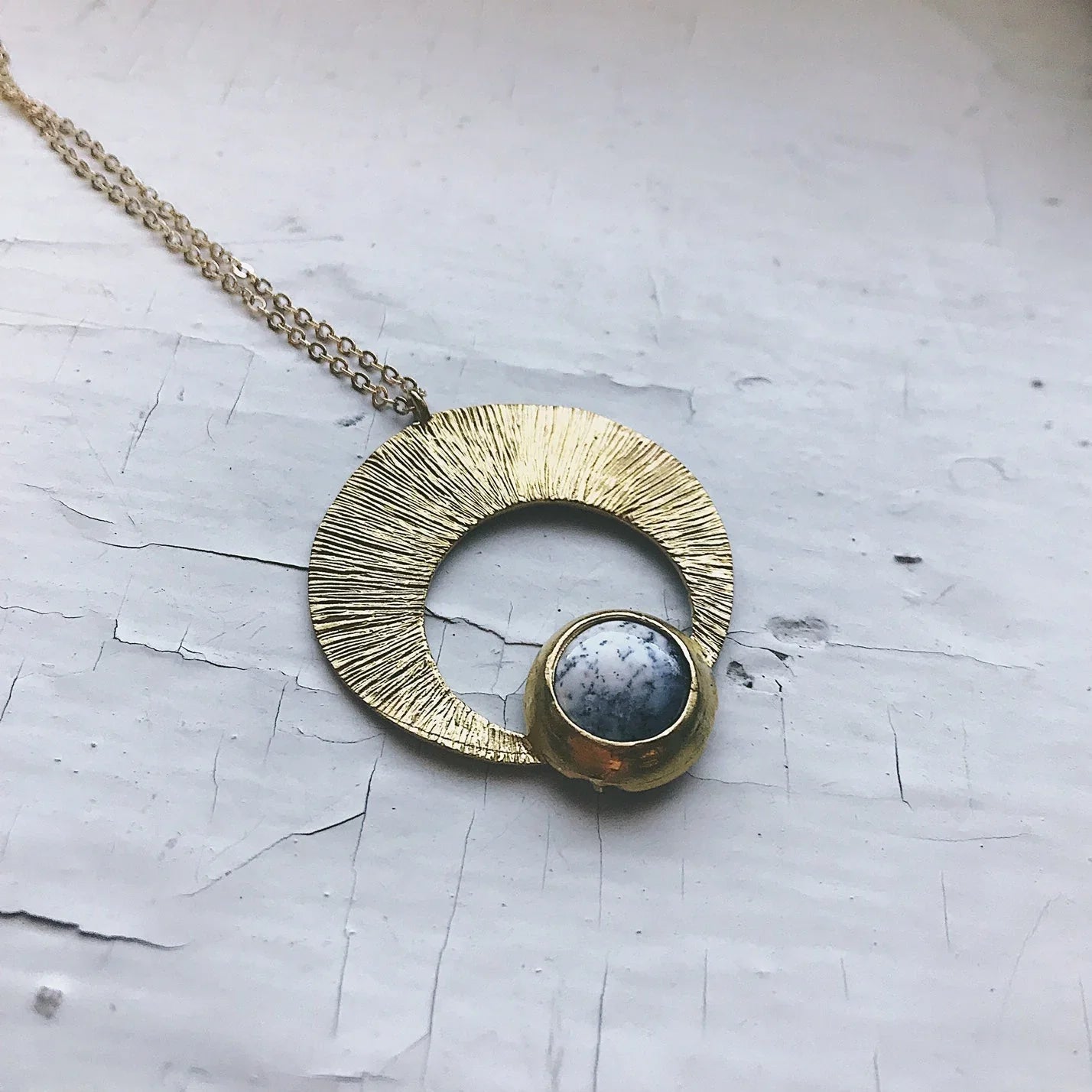 Gold crescent pendant necklace with marbled stone on textured white background