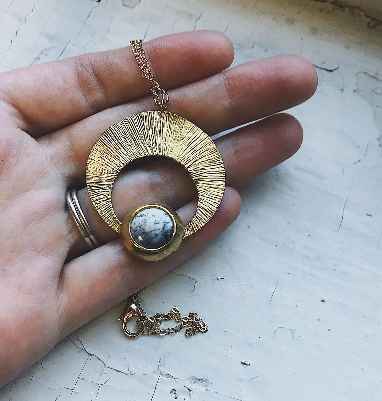 Hand holding crescent pendant necklace with gold textured circle and white marble stone, Qu!rk Boutique