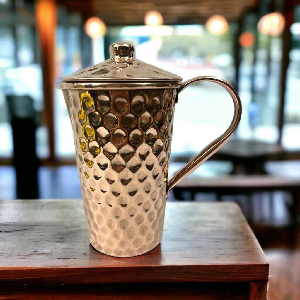 Hammered metal pitcher with lid on wooden table, boutique gift shop background