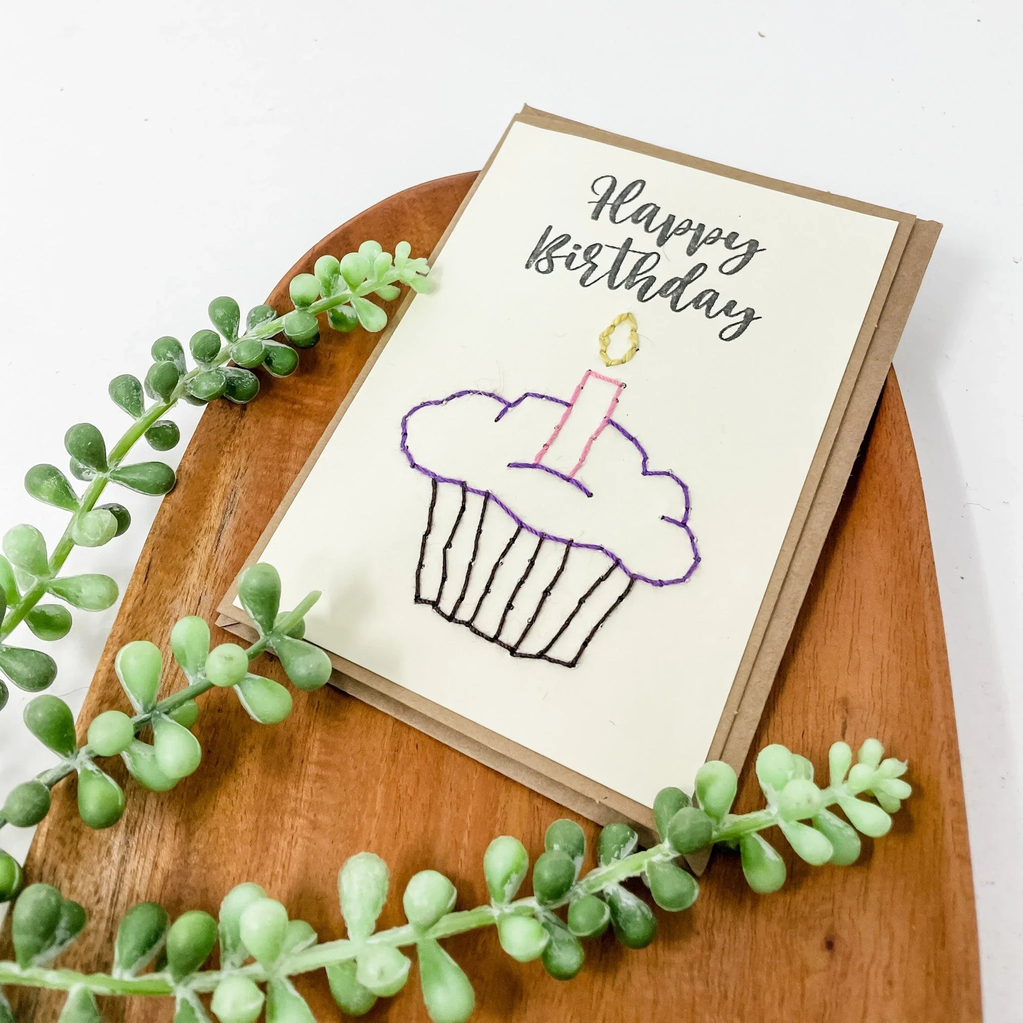 Handmade Happy Birthday card with cupcake illustration, displayed on wooden tray with greenery
