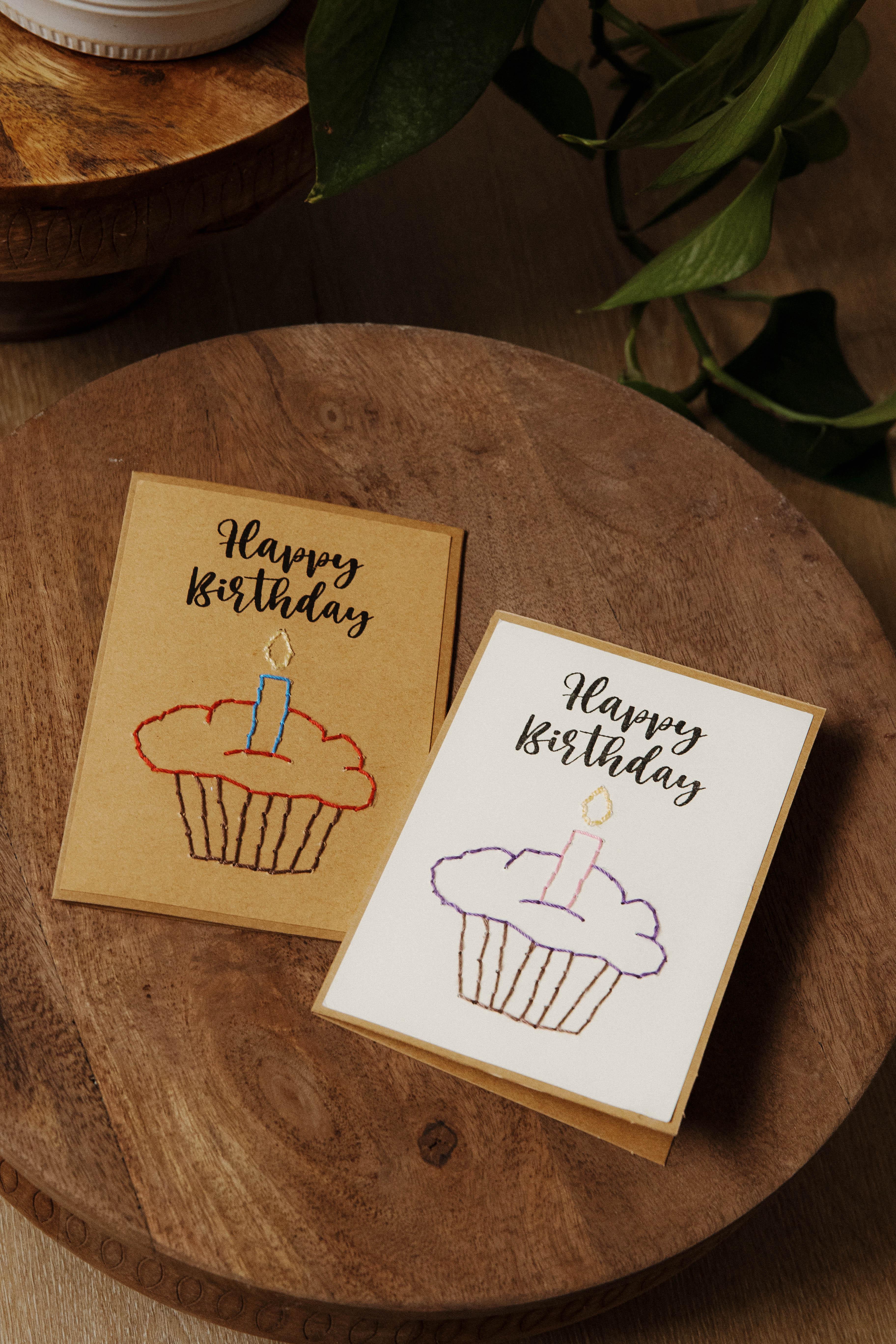 Handmade birthday cards with embroidered cupcake design on a wooden table at Qu!rk Boutique