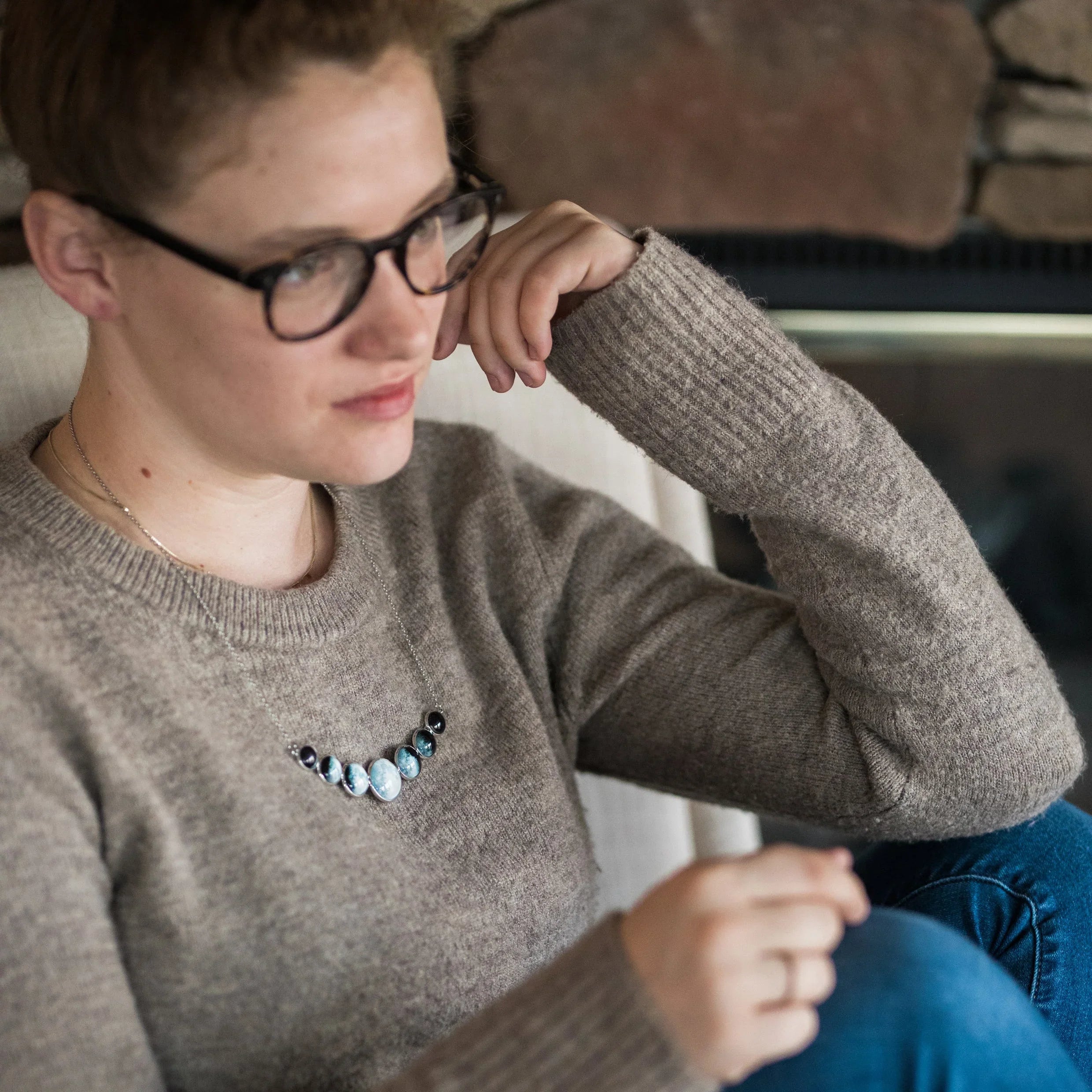 Woman wearing glasses and gray sweater sitting indoors with a multi-stone blue and black necklace