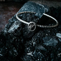 Handcrafted silver bracelet with a dark crystal centerpiece on black rocky stones, Qu!rk Boutique